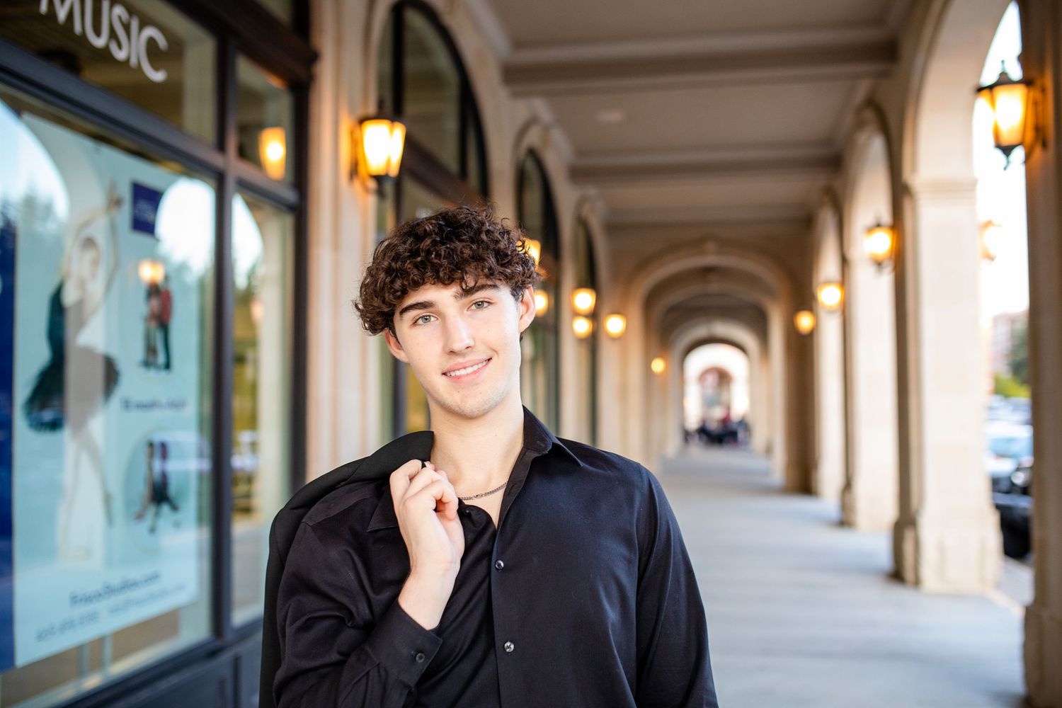 A person stands smiling in a classic covered colonnade with warm lighting and arched architecture.