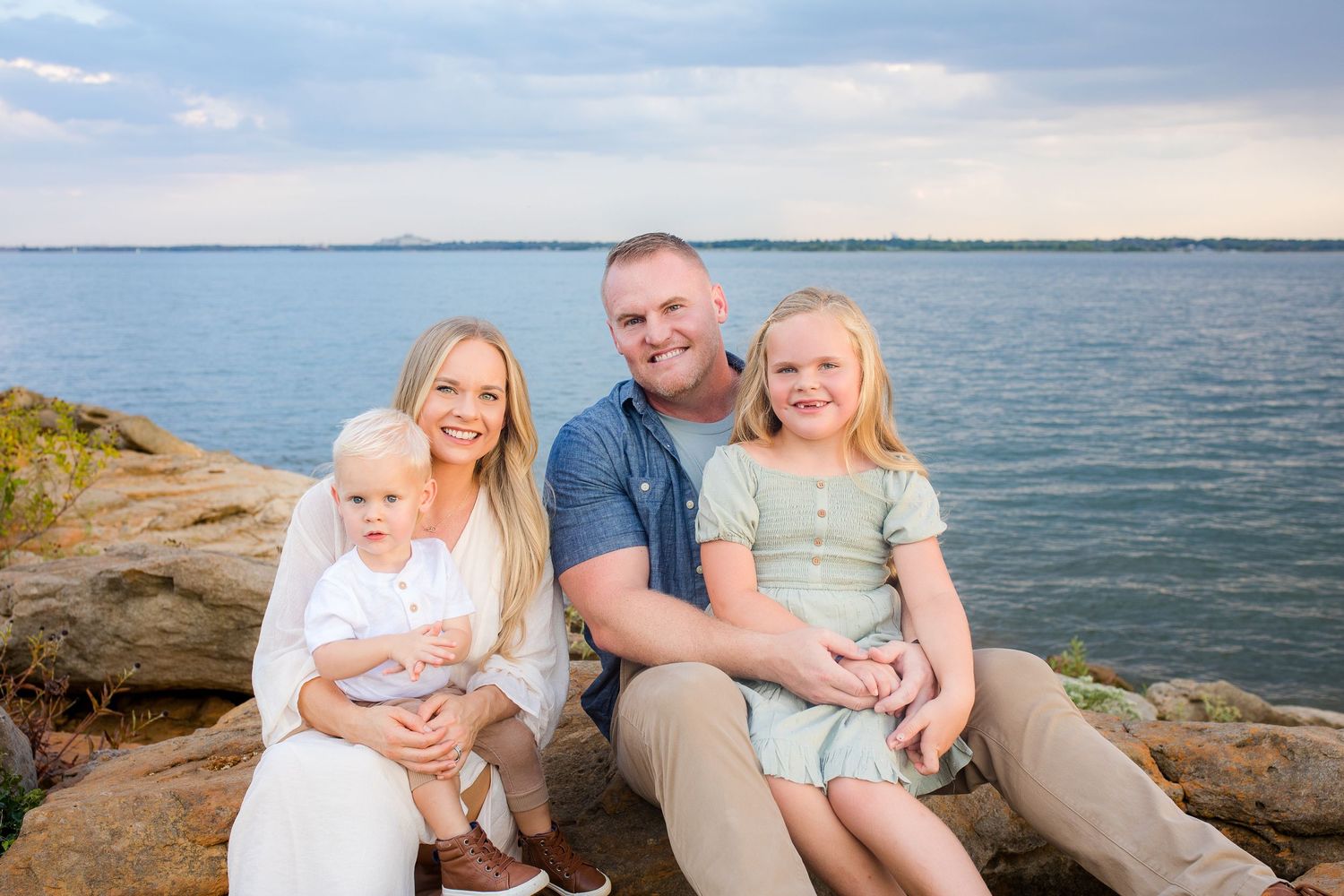 A family enjoys relaxing together on coastal rocks overlooking the ocean at sunset.