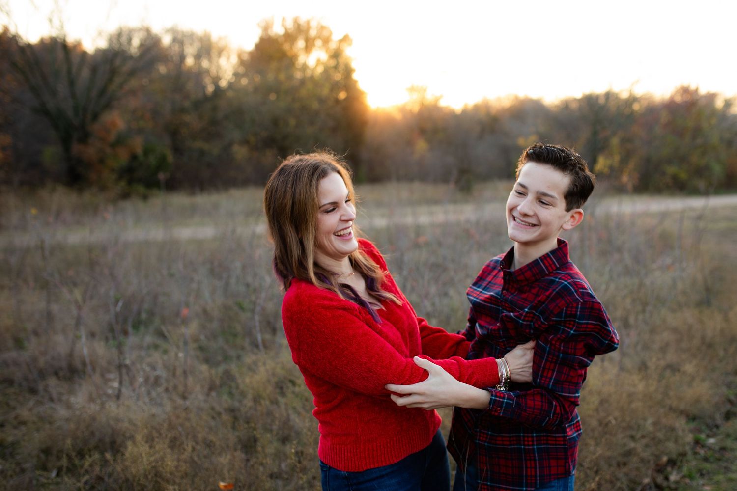 Two people share a joyful moment together in a field during sunset, wearing red and plaid sweaters.