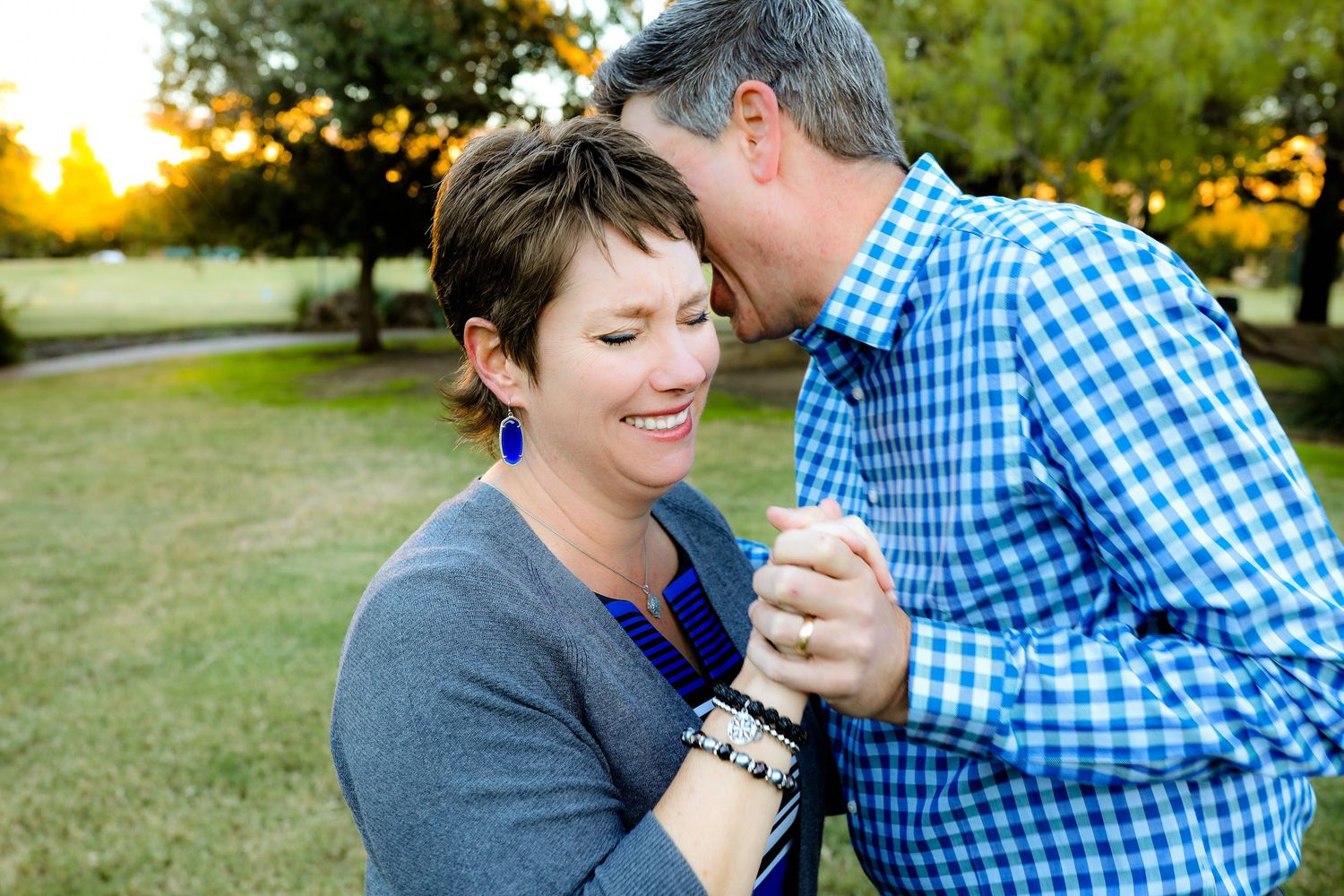 A couple dances together in a park during golden hour while holding hands and smiling.