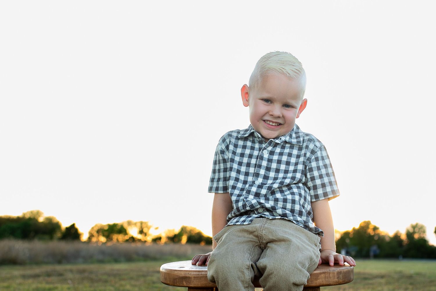 A little one in a checkered shirt sits outdoors at sunset during a golden hour family photo session.