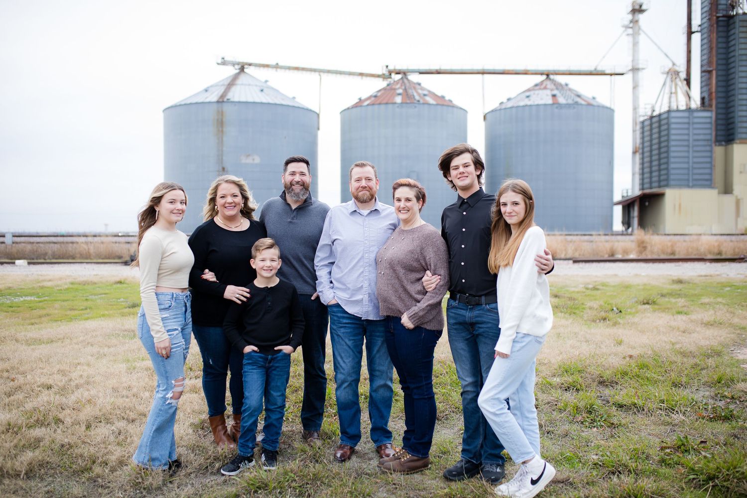 A group enjoying a casual gathering in front of grain storage silos on a rural farm property.