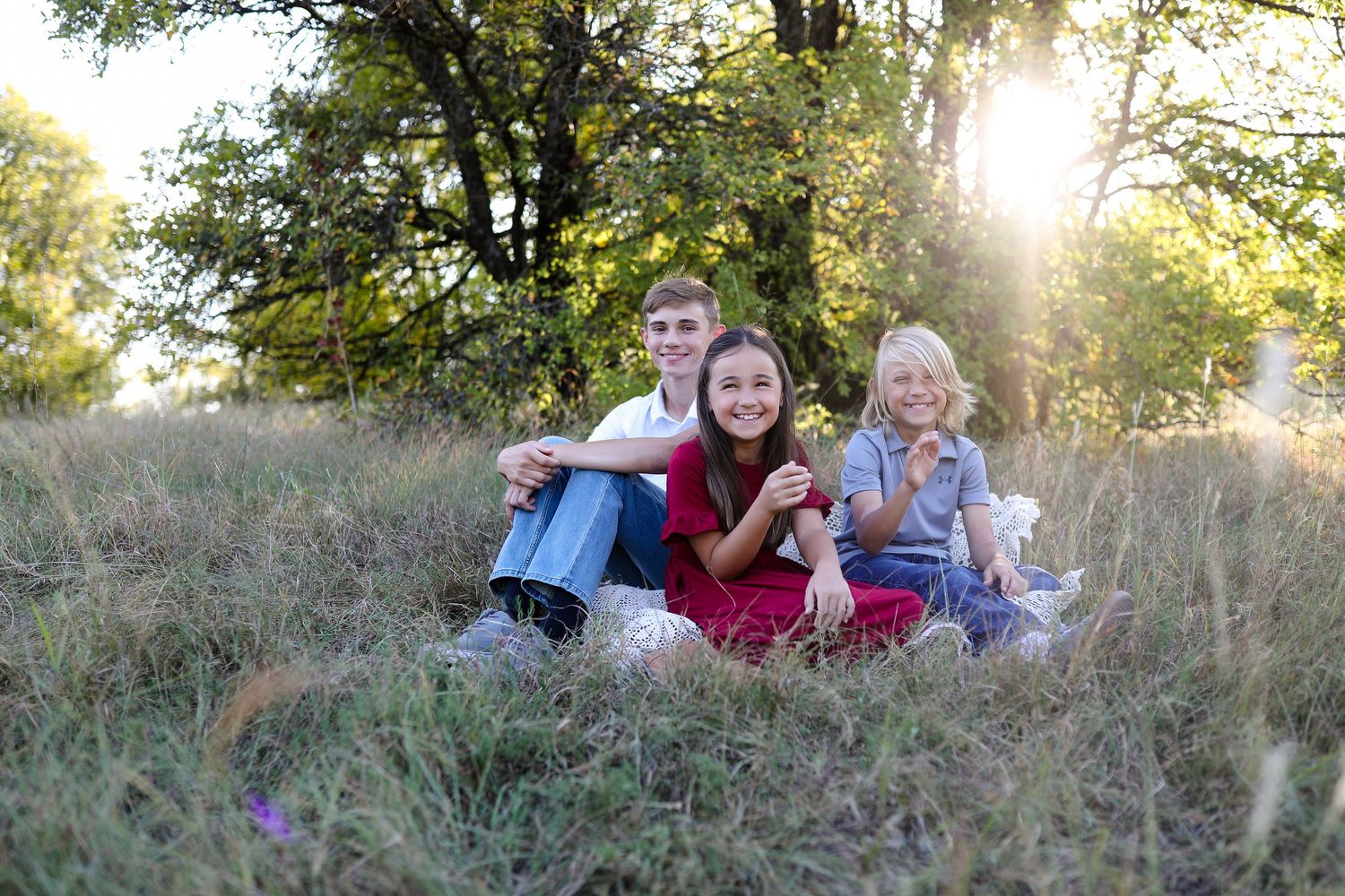 A group enjoying a casual outdoor photoshoot together on a grassy hillside at golden hour.