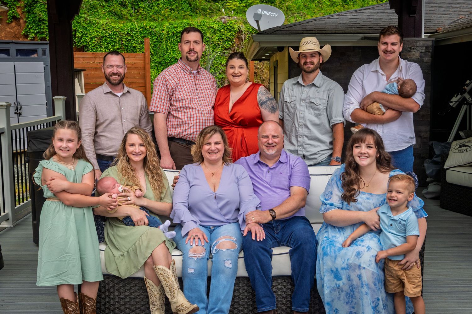 A large multi-generational family group poses together outdoors on a porch for a casual photo gathering.