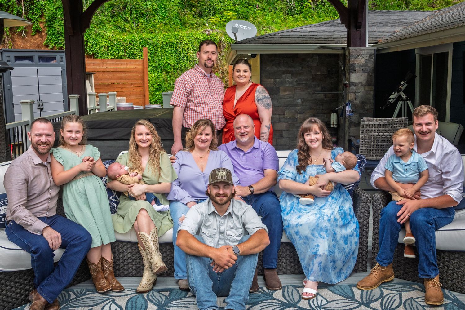 Family members wearing casual outfits gather together on front porch steps for photos on a sunny day.