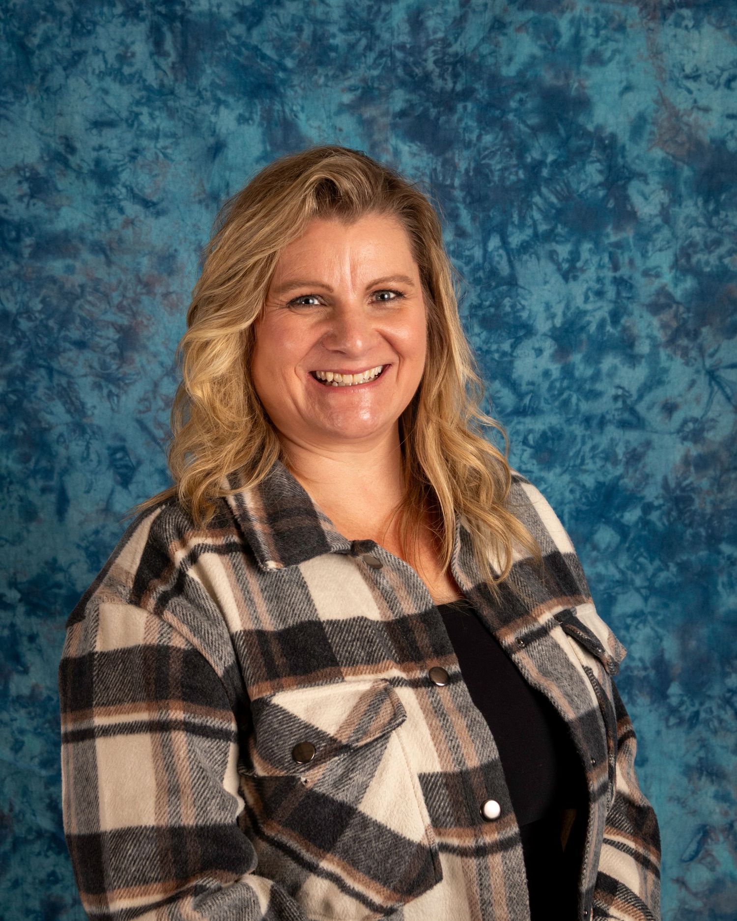 Professional portrait of someone wearing a black and white plaid flannel shirt against a textured blue backdrop.
