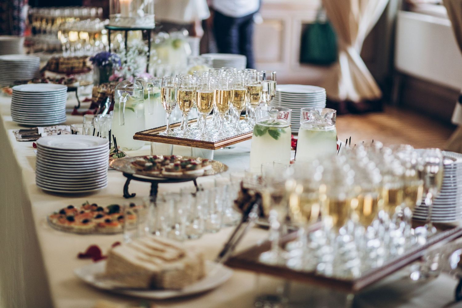 A long banquet table is elegantly set with glasses, plates, and appetizers for a formal dining event.