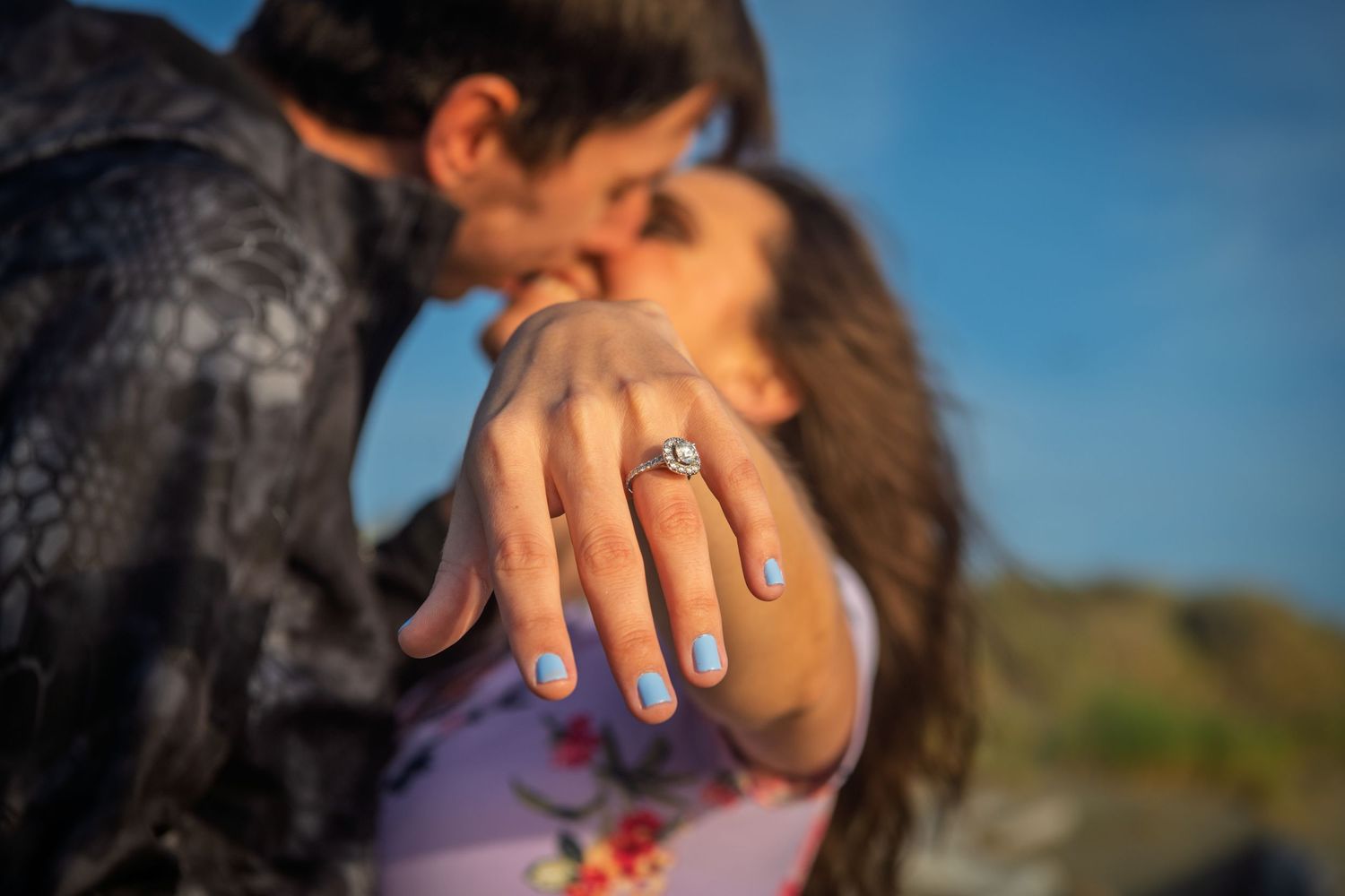 Romantic engagement photo highlighting diamond ring as couple celebrates proposal outdoors.