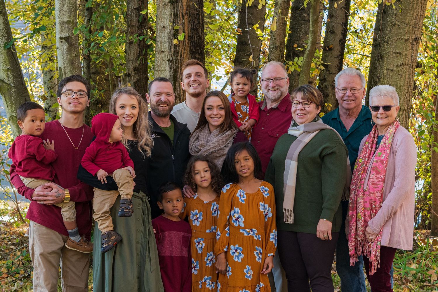 Large group of people wearing red and casual attire pose together outdoors among autumn trees for a group photo.