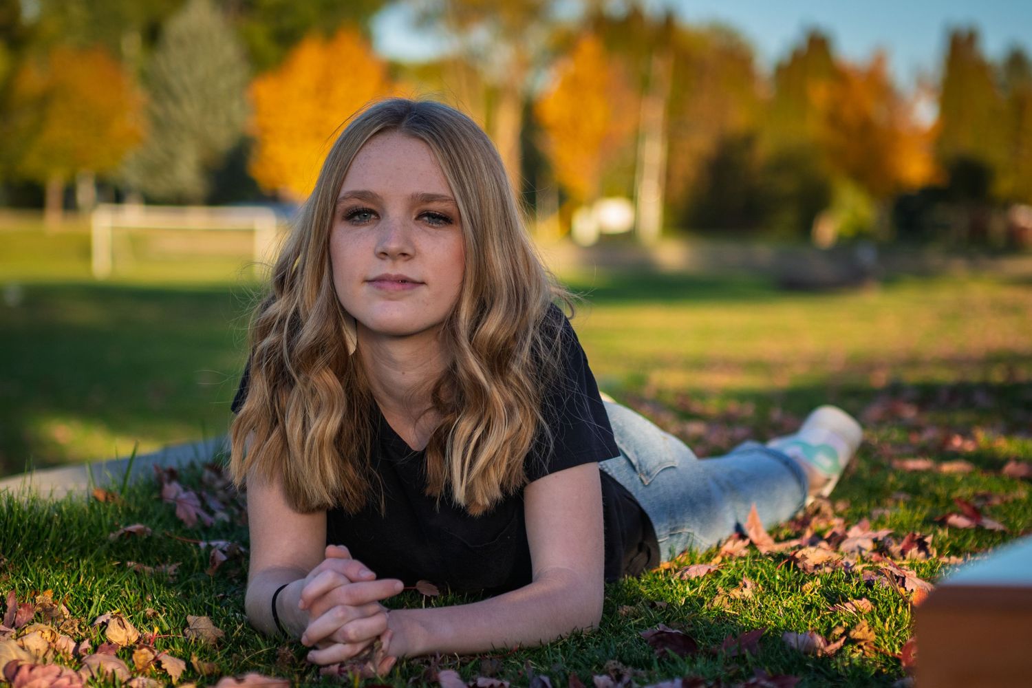Person lying in autumn leaves during golden hour sunset creating artistic outdoor portrait series.