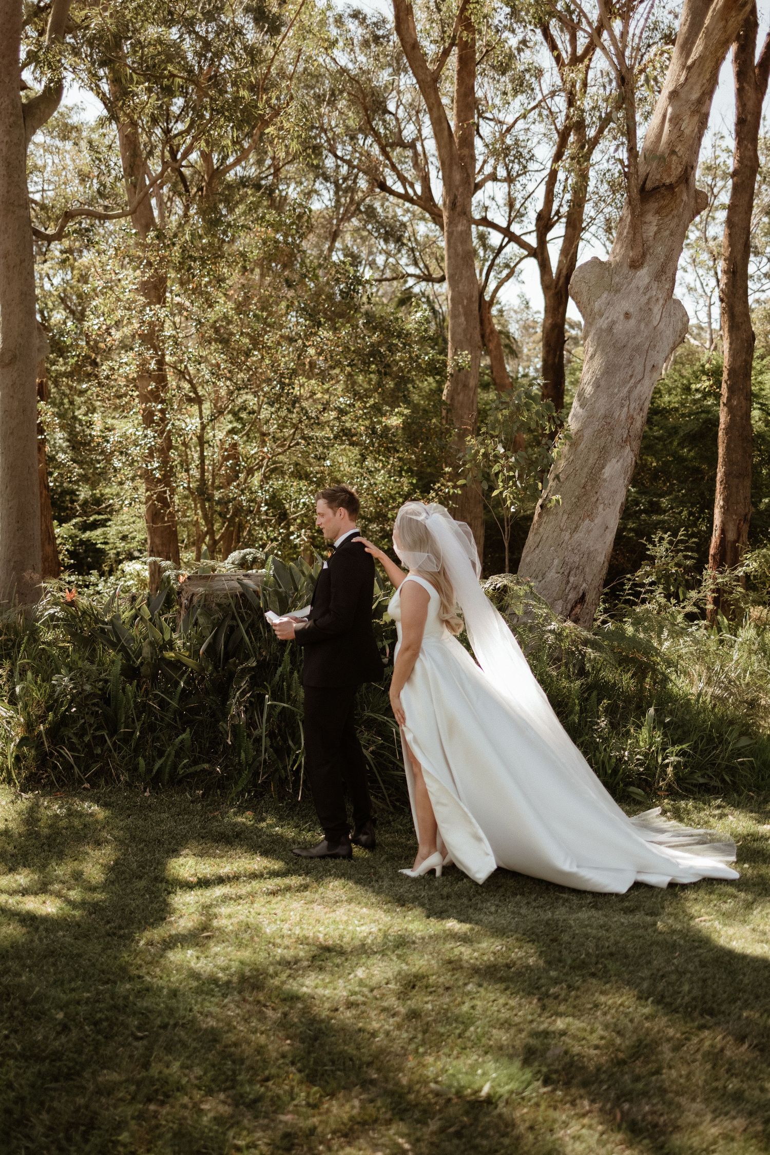 Bride and groom share an intimate moment reading vows in a lush green outdoor garden setting.