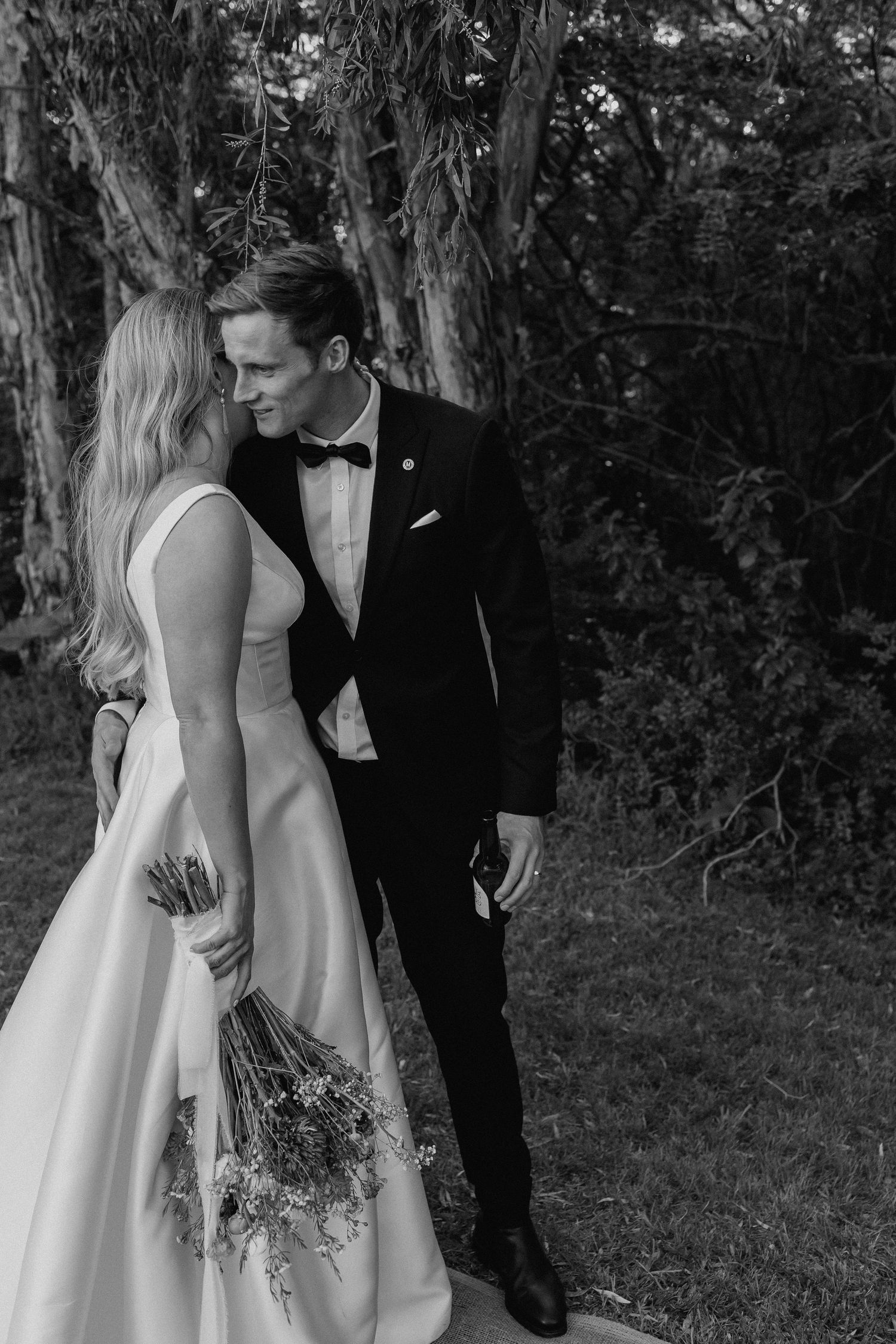 Black and white romantic portrait of bride and groom standing close together in a garden setting.