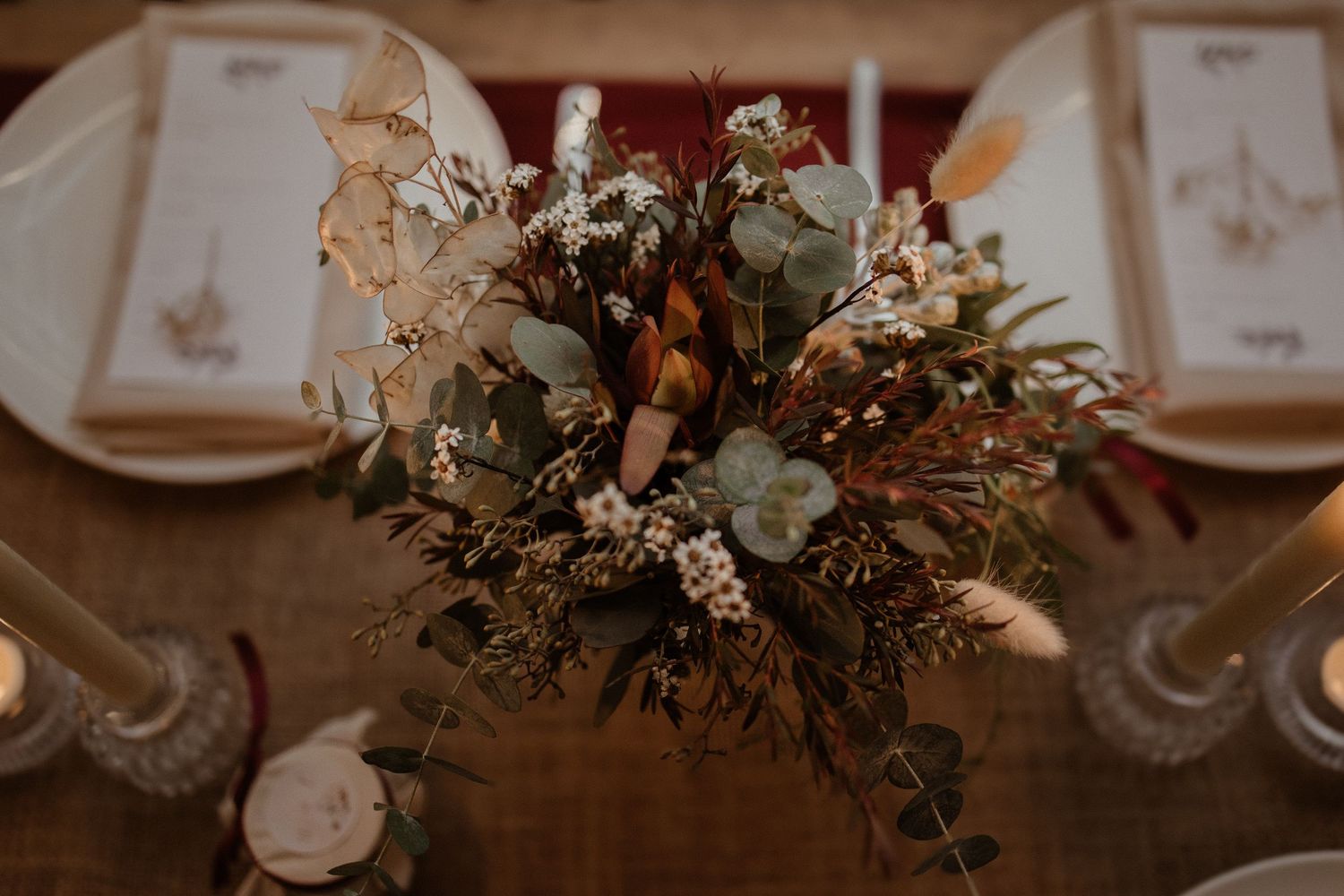 Rustic wedding table centerpiece featuring protea, eucalyptus, and dried flowers with candles.