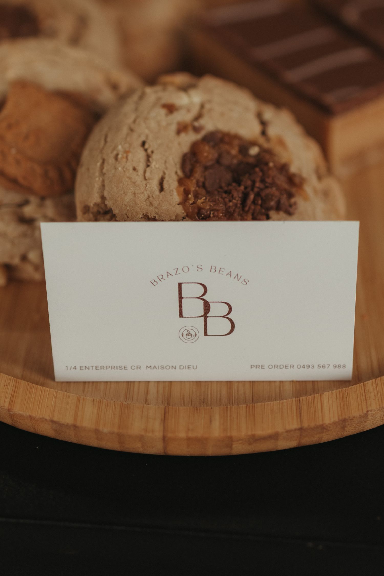 Brazo's Beans BB business card displayed in front of chocolate chip cookies on a wooden board.