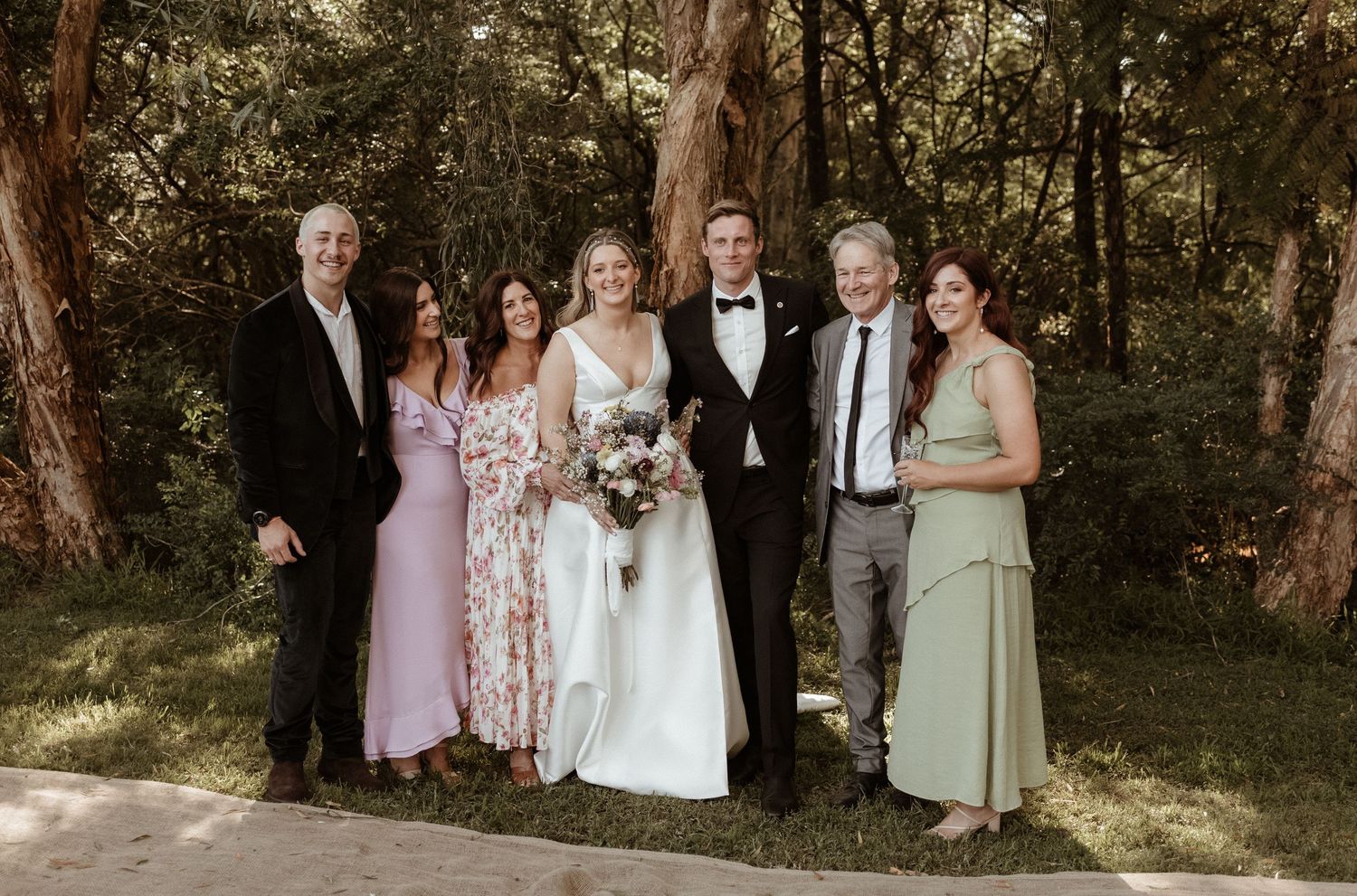 Wedding party group portrait with bride and groom and four guests in woodland setting.