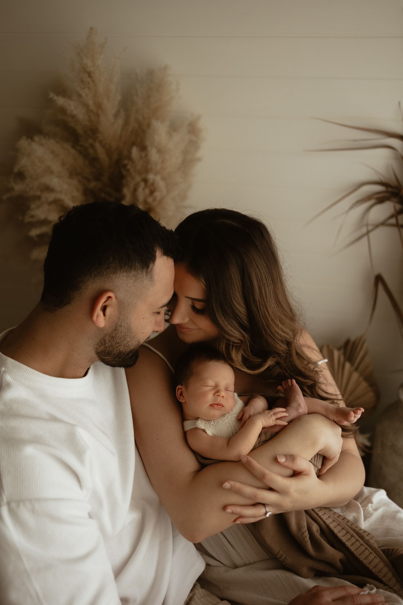 Young parents lovingly gaze at sleeping newborn baby in warm boho-styled photo session.
