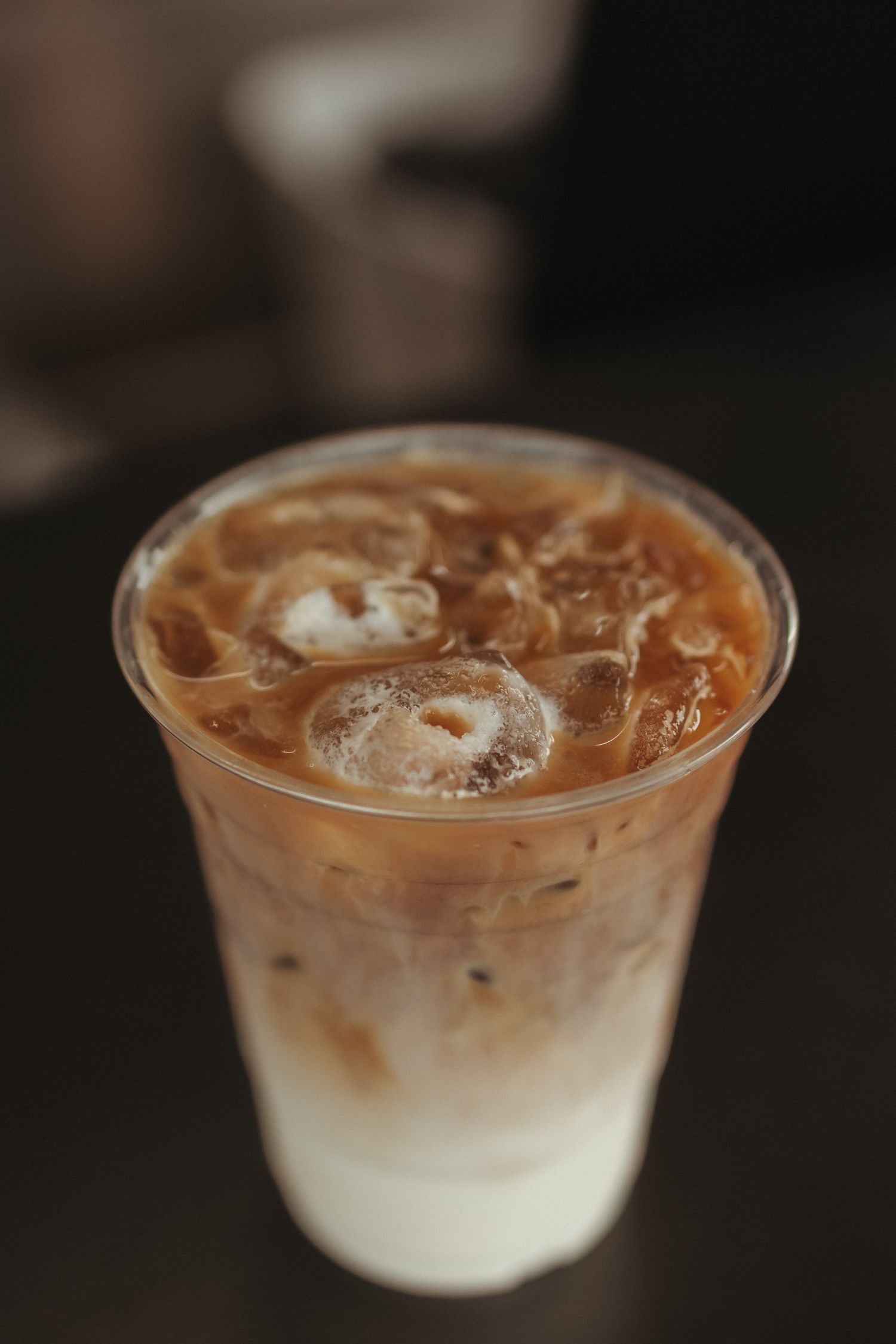 Close-up of a creamy iced latte in a clear plastic cup with swirling milk and coffee on dark surface.