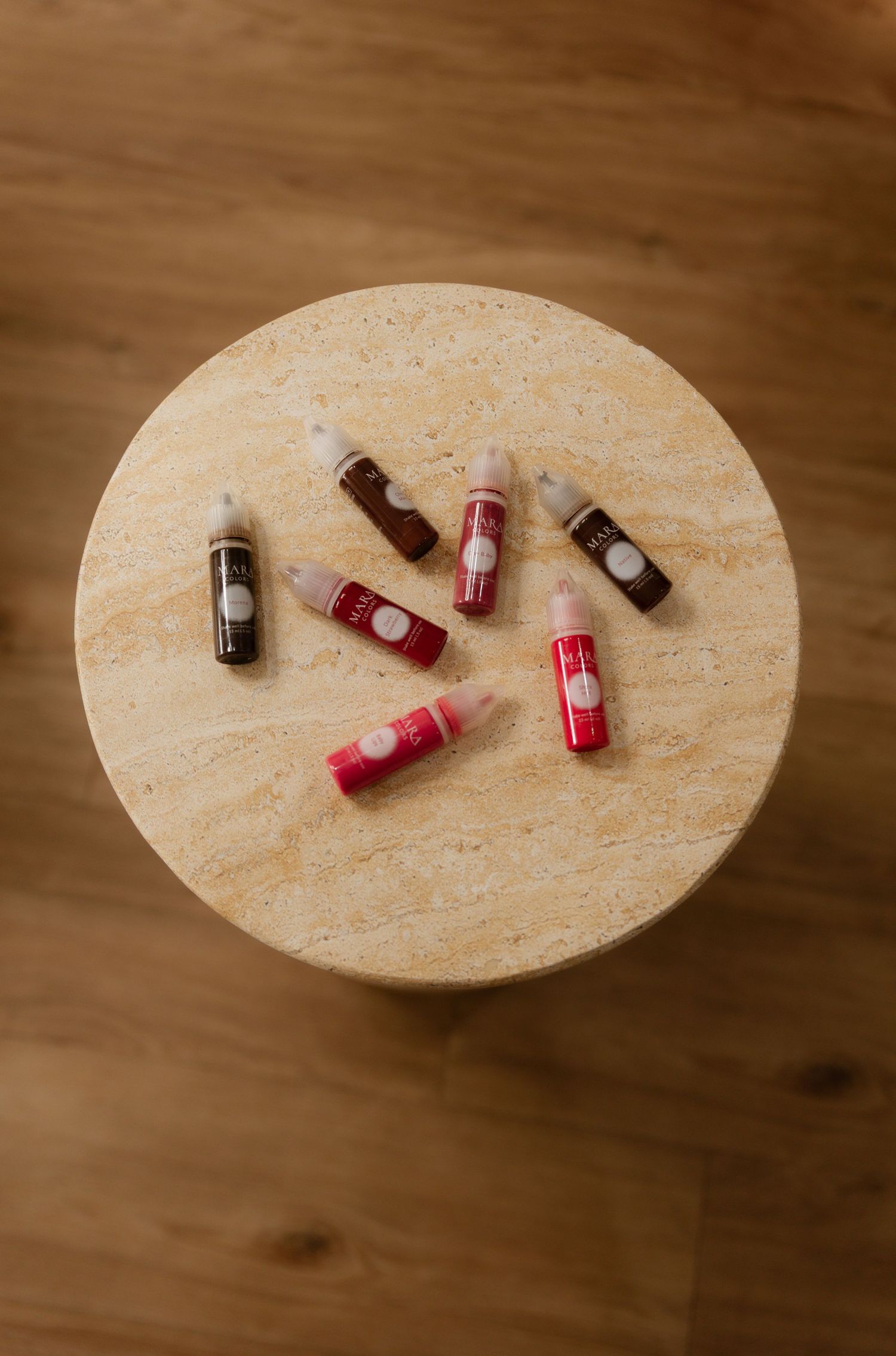 Collection of red and brown lip gloss bottles arranged on a round marble side table.