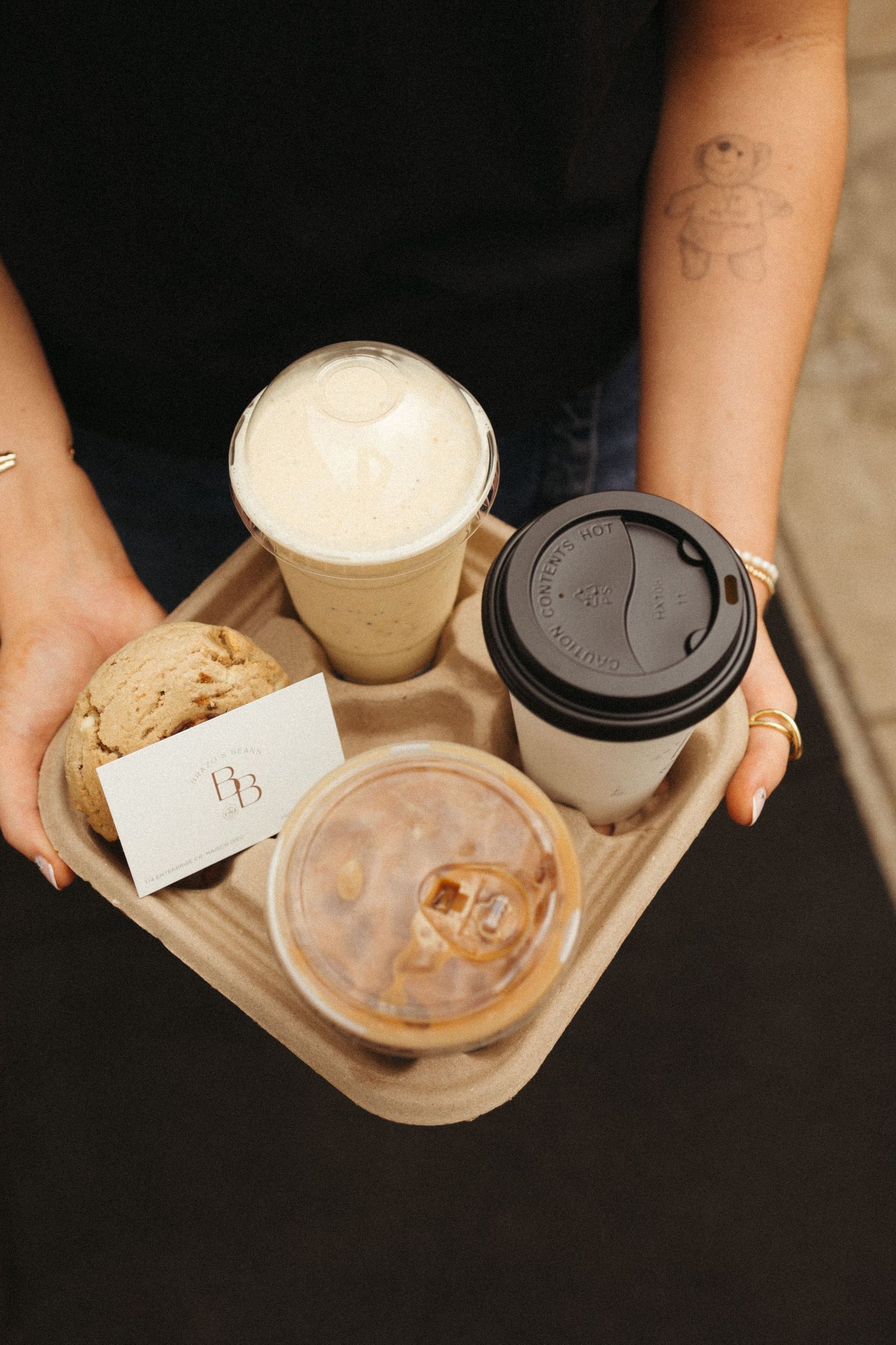 Person holding a cardboard tray with iced coffee, hot coffee, a latte, and a branded business card.