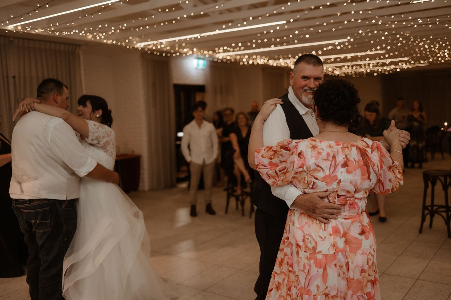 Couples share romantic dances on a wedding reception dance floor adorned with twinkling fairy lights.