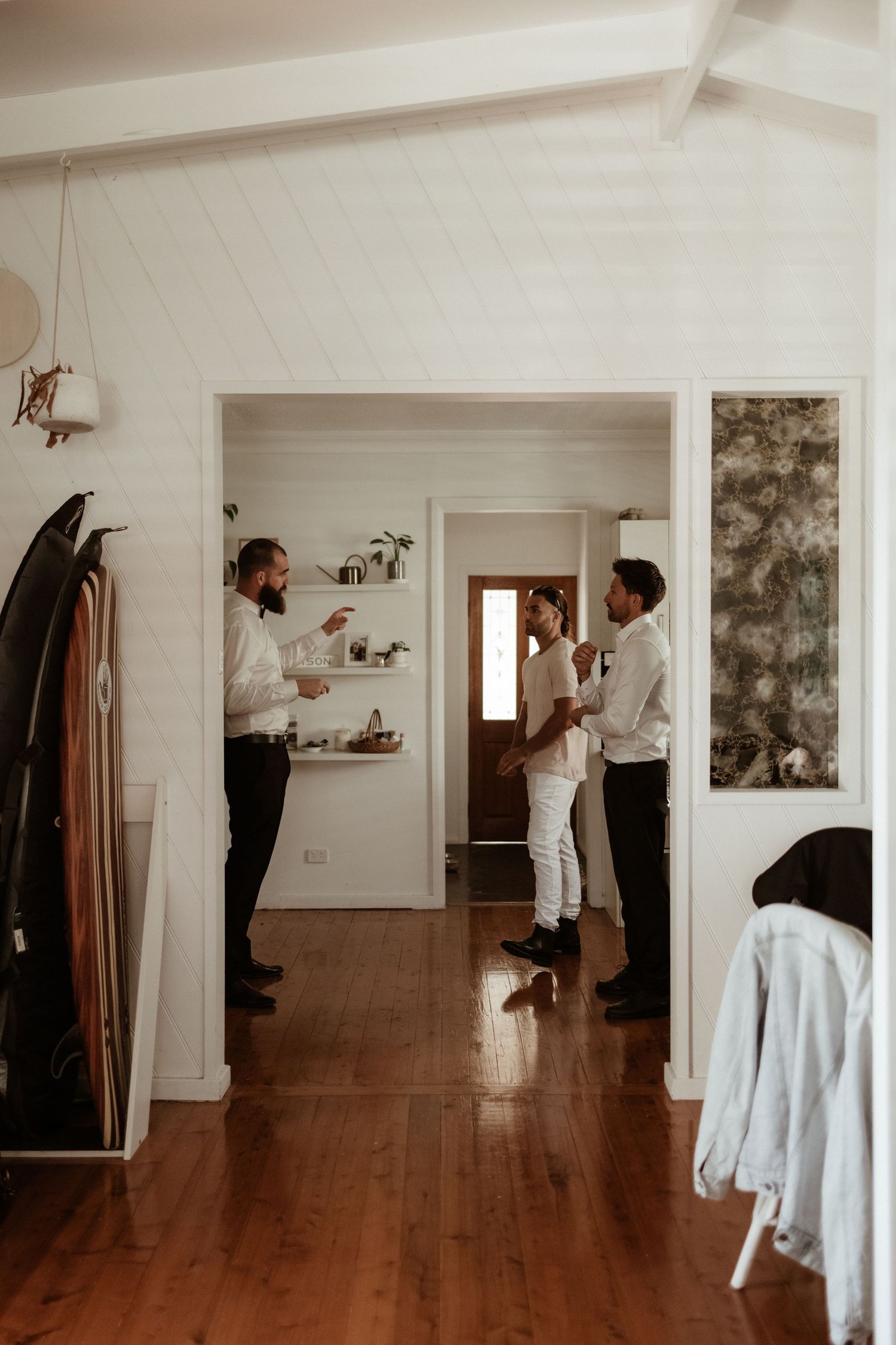 Groomsmen chatting in a white coastal home before a wedding ceremony.