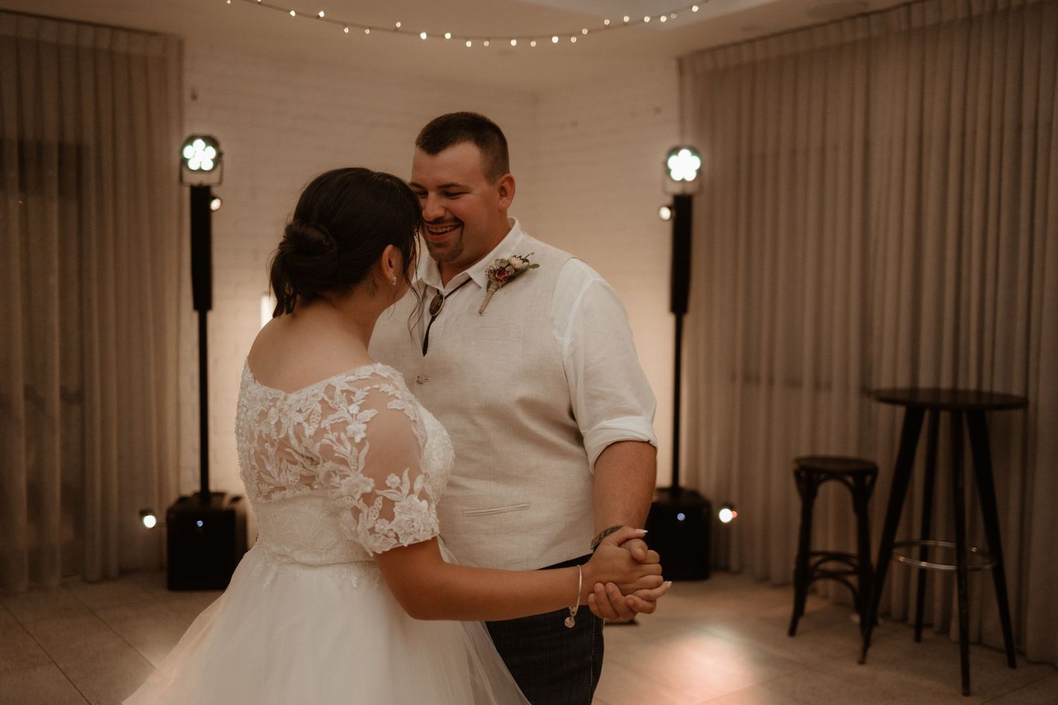 Bride and groom share romantic first dance together under soft warm lighting at wedding reception.