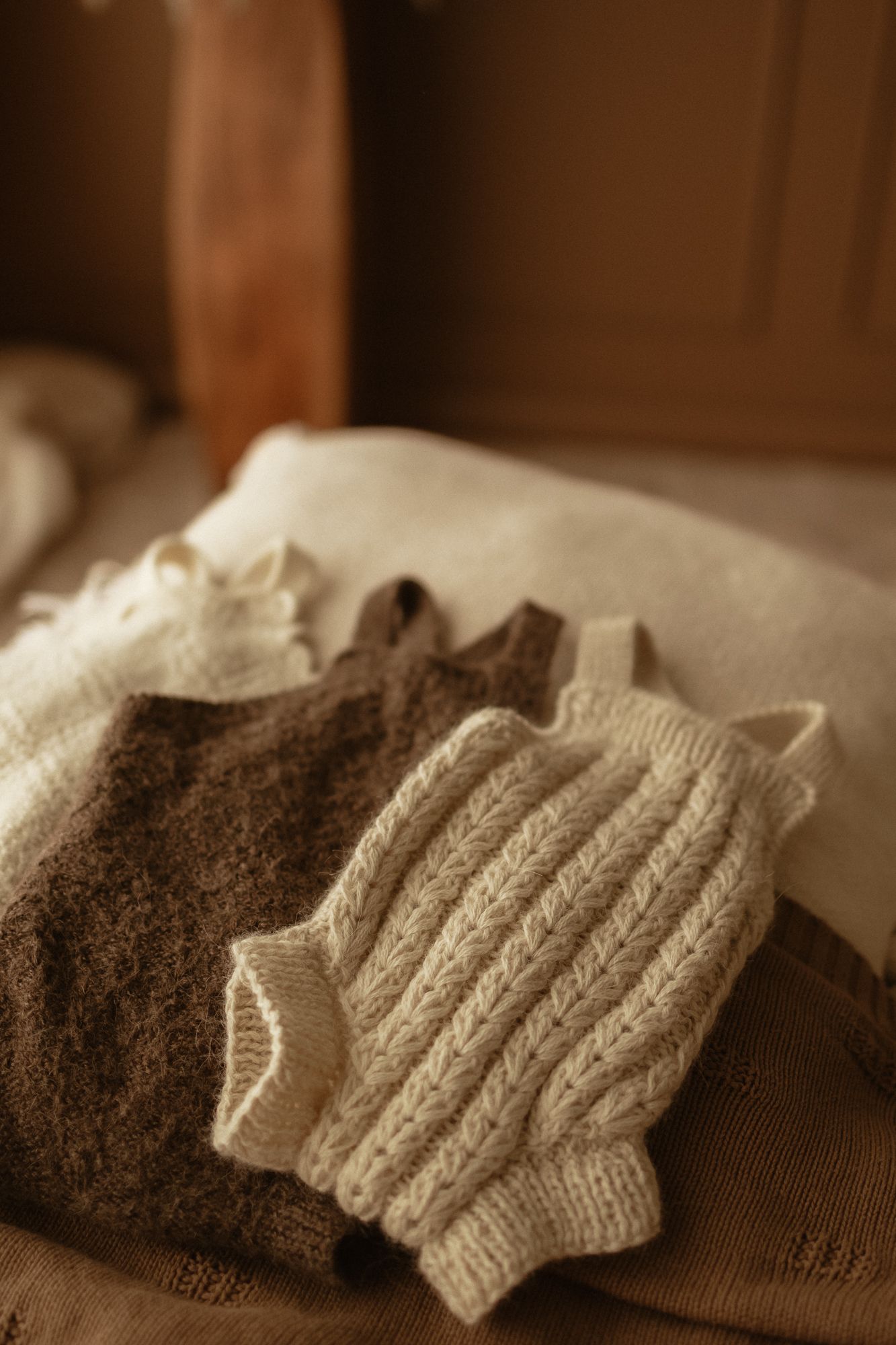 Cozy knit baby rompers in cream and brown tones arranged on a warm neutral surface.