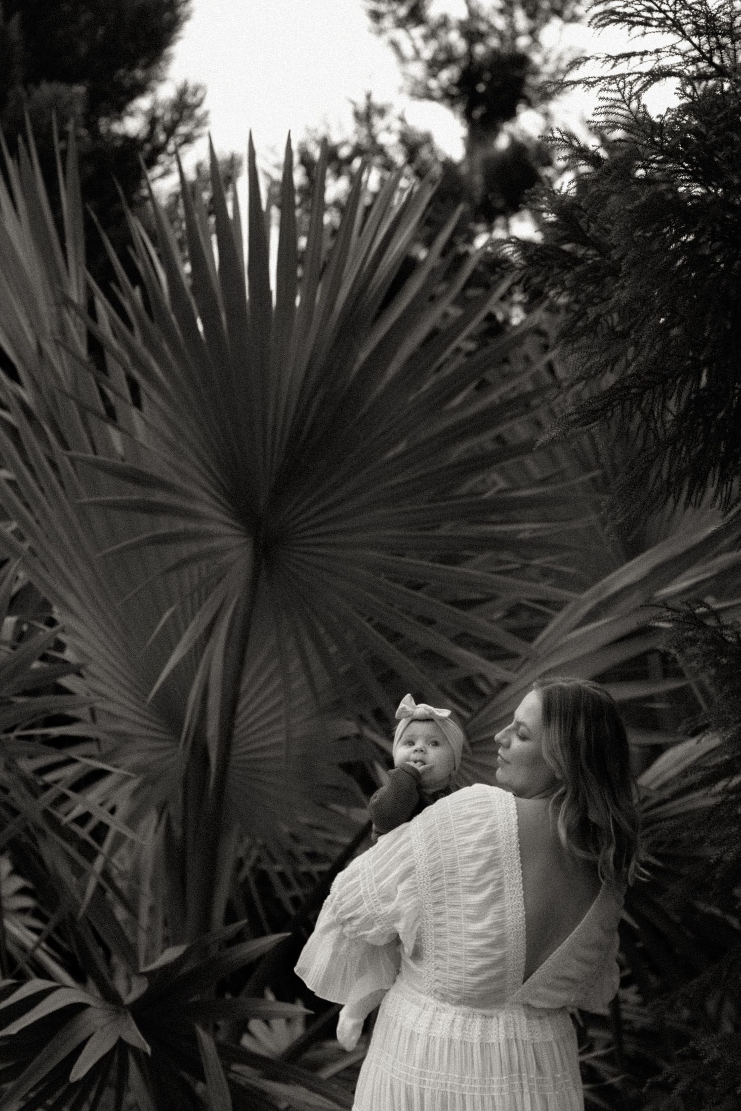 Black and white photo of mother holding baby among fan palm trees.