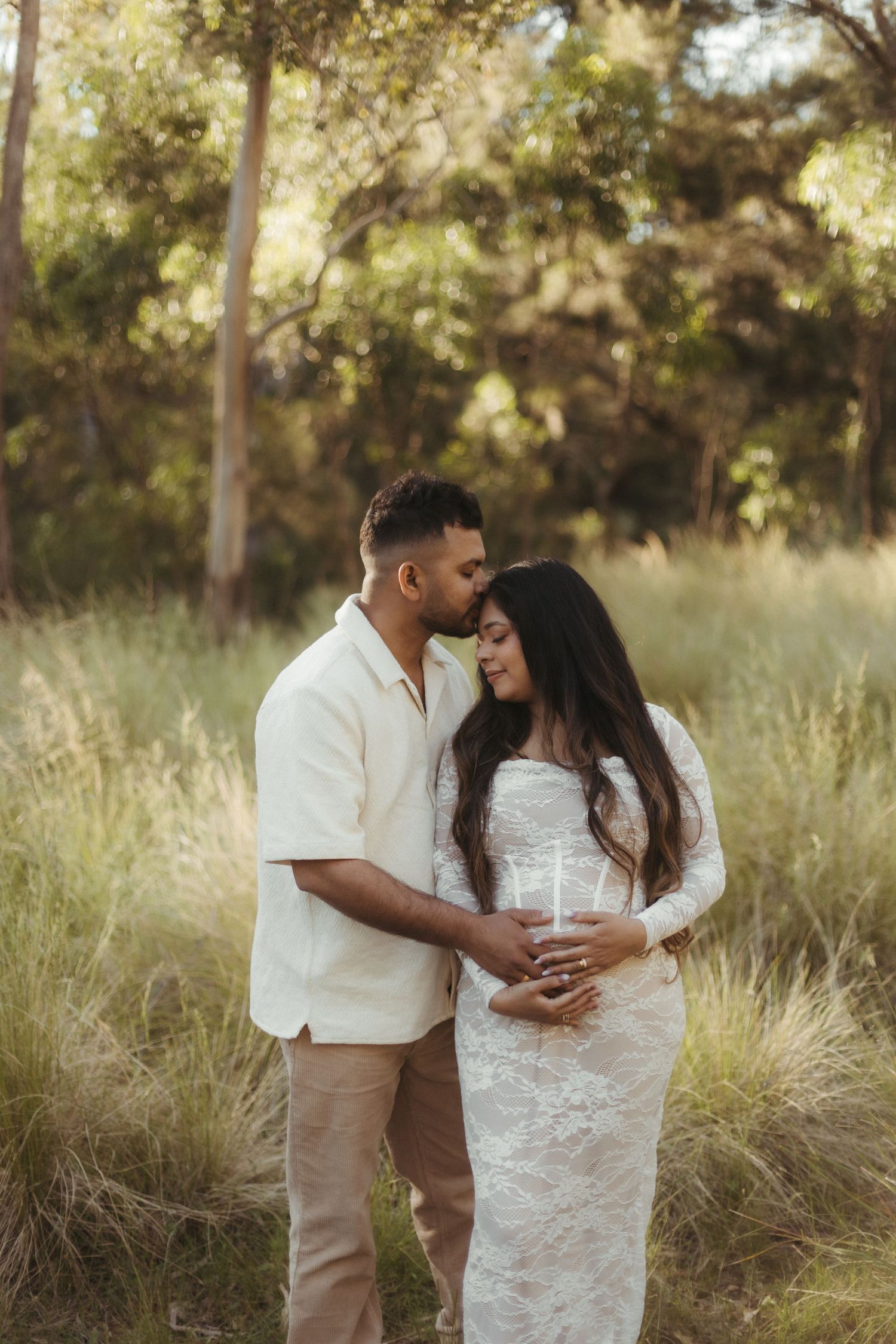 Couple embracing in tall grass field during golden hour maternity photography session.