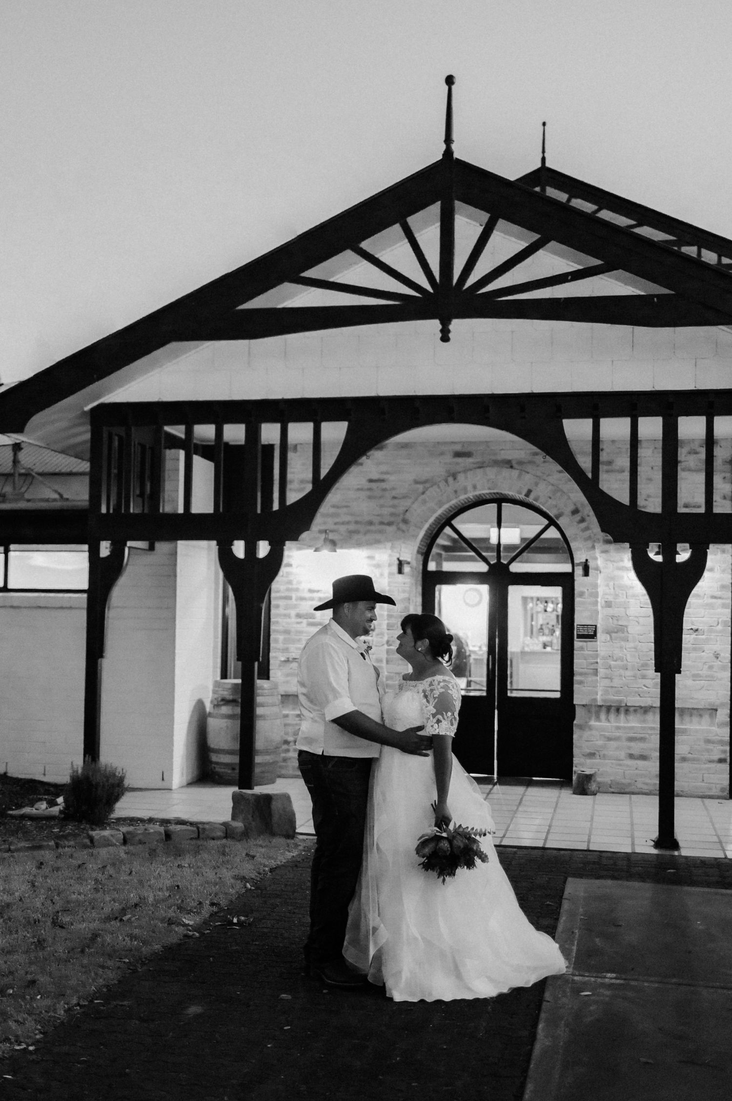 Bride and groom sharing romantic moment outside historic stone building in black and white.