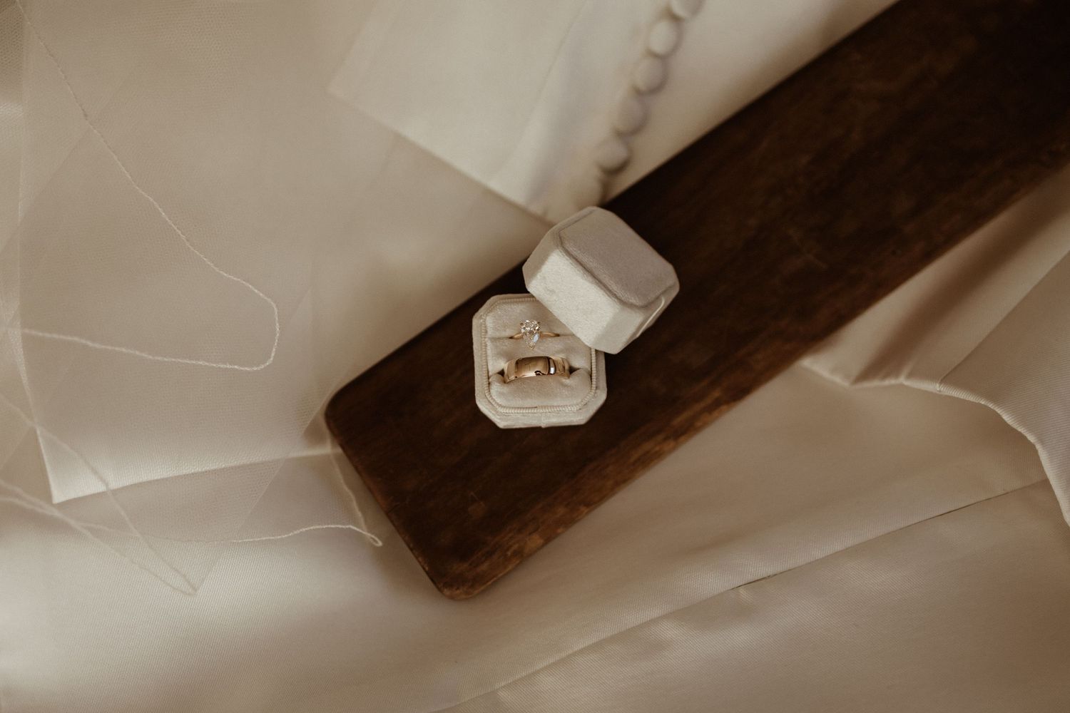 Gold wedding rings displayed in a white velvet ring box on a dark wooden surface with silk fabric.