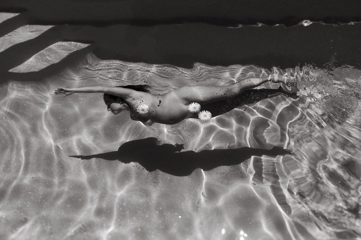 Black and white aerial view of a woman swimming underwater in a clear pool.