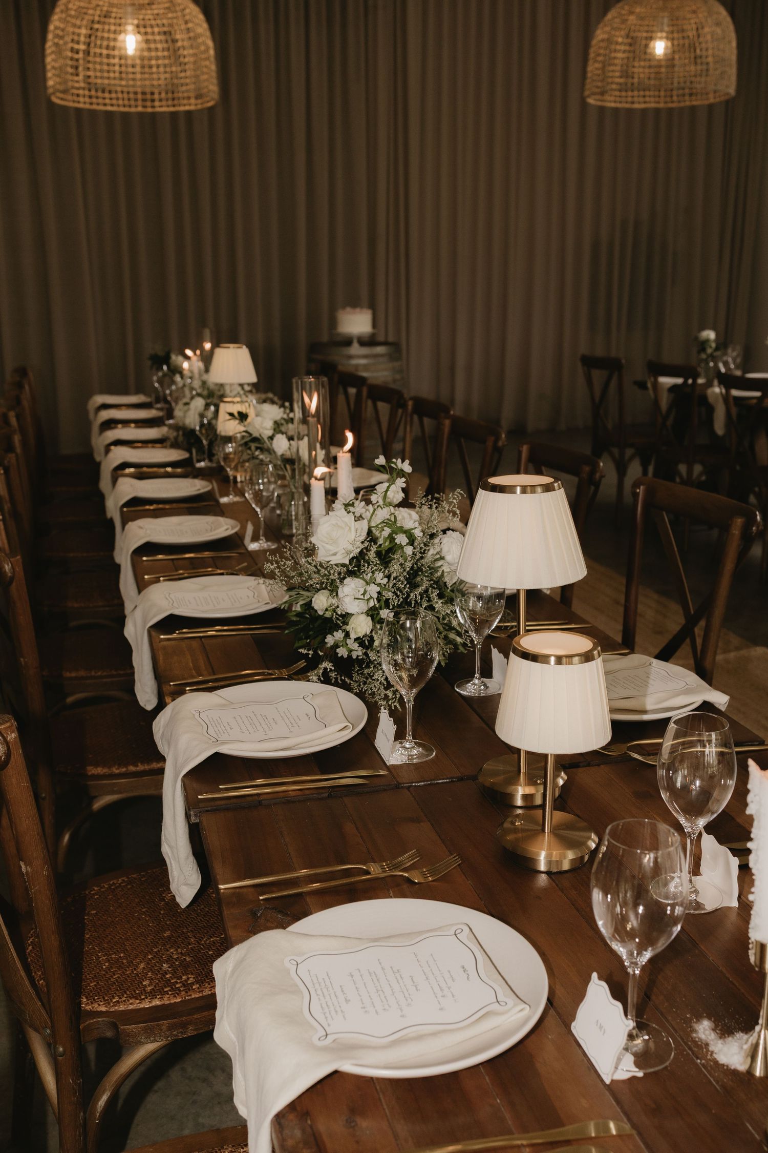 Elegant wedding reception table set with white plates, candles, floral centerpieces, and gold accents.