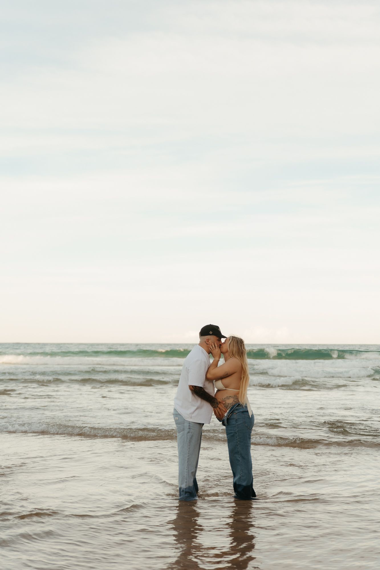 Romantic couple embracing and kissing on a sandy beach with ocean waves in the background.