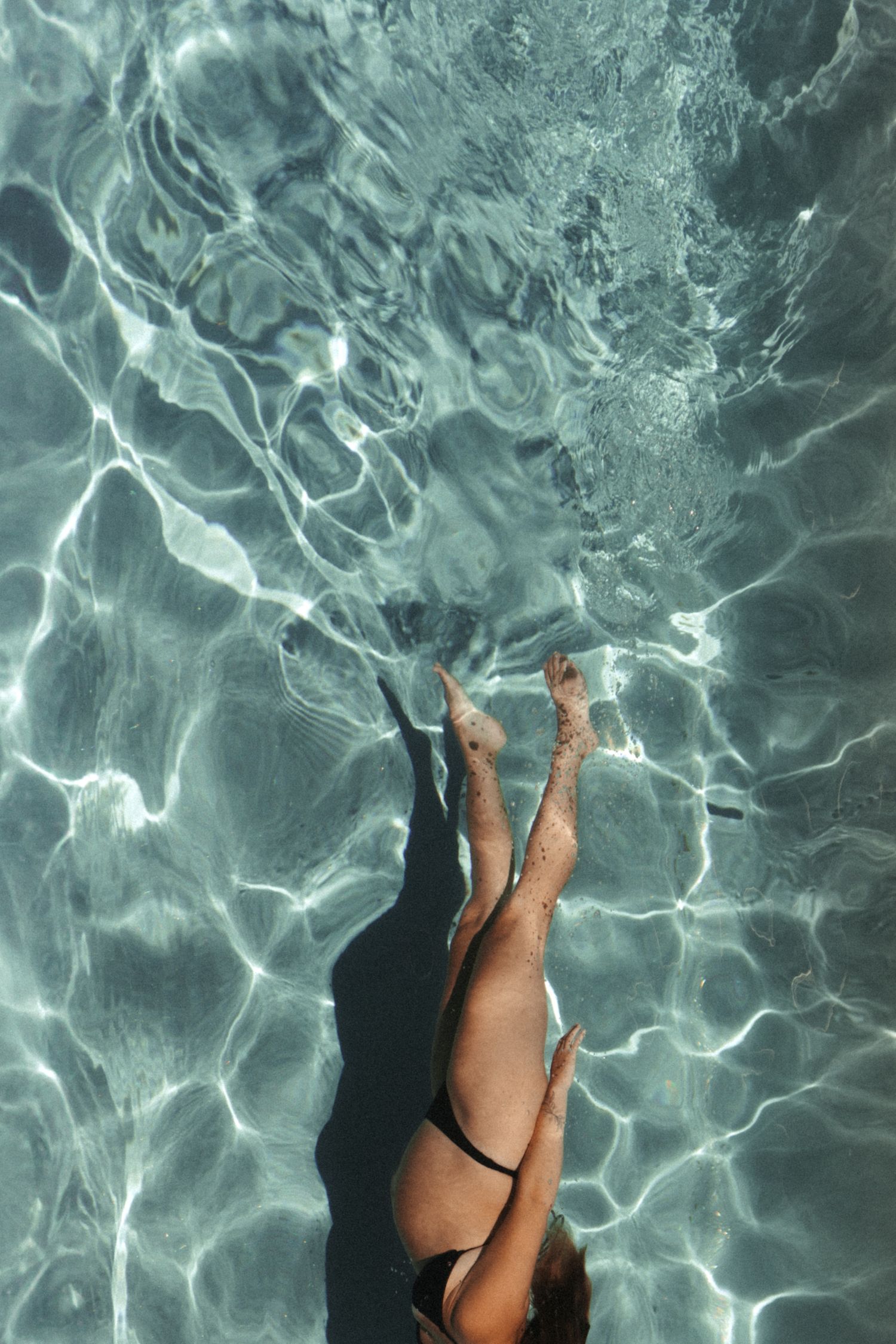 Overhead view of woman diving into sparkling clear swimming pool.