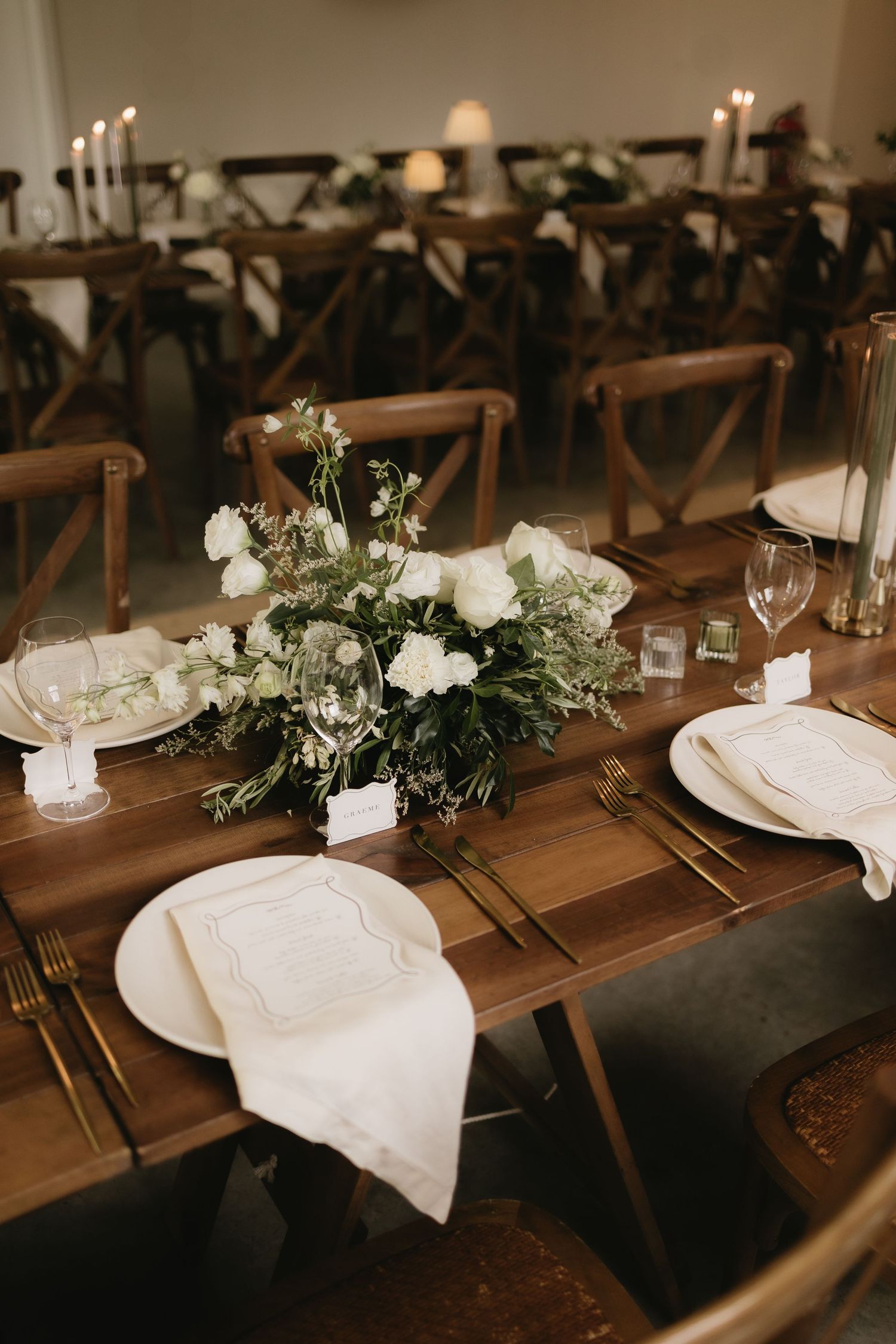 Elegant rustic wedding reception tables with white roses and greenery centerpieces.