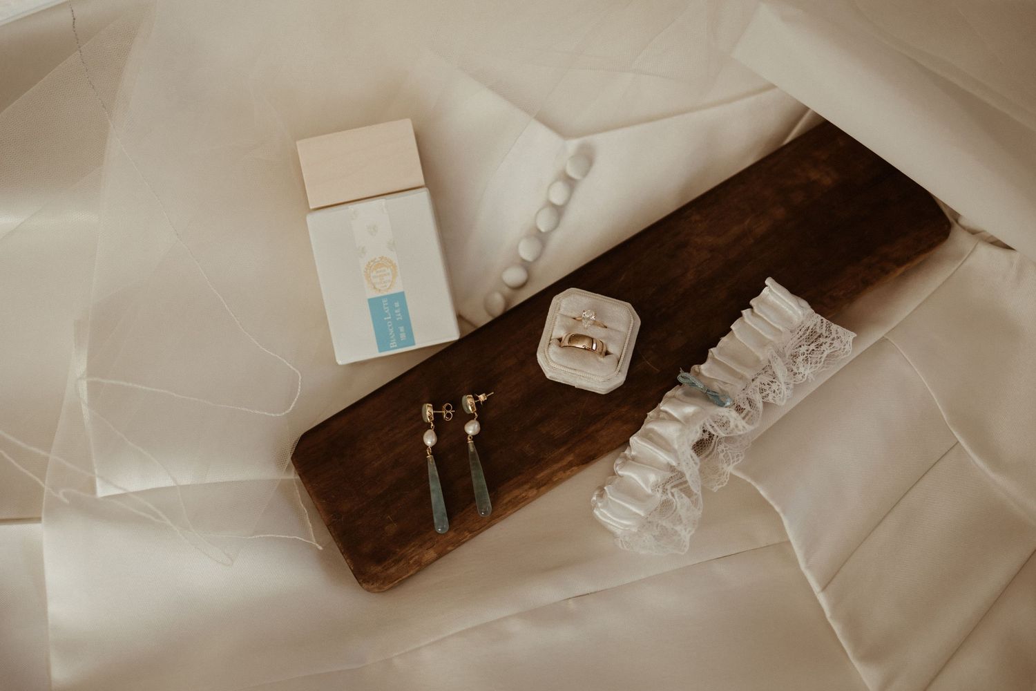 Flat lay of wedding accessories including rings, earrings, a garter, and bracelet on white fabric.