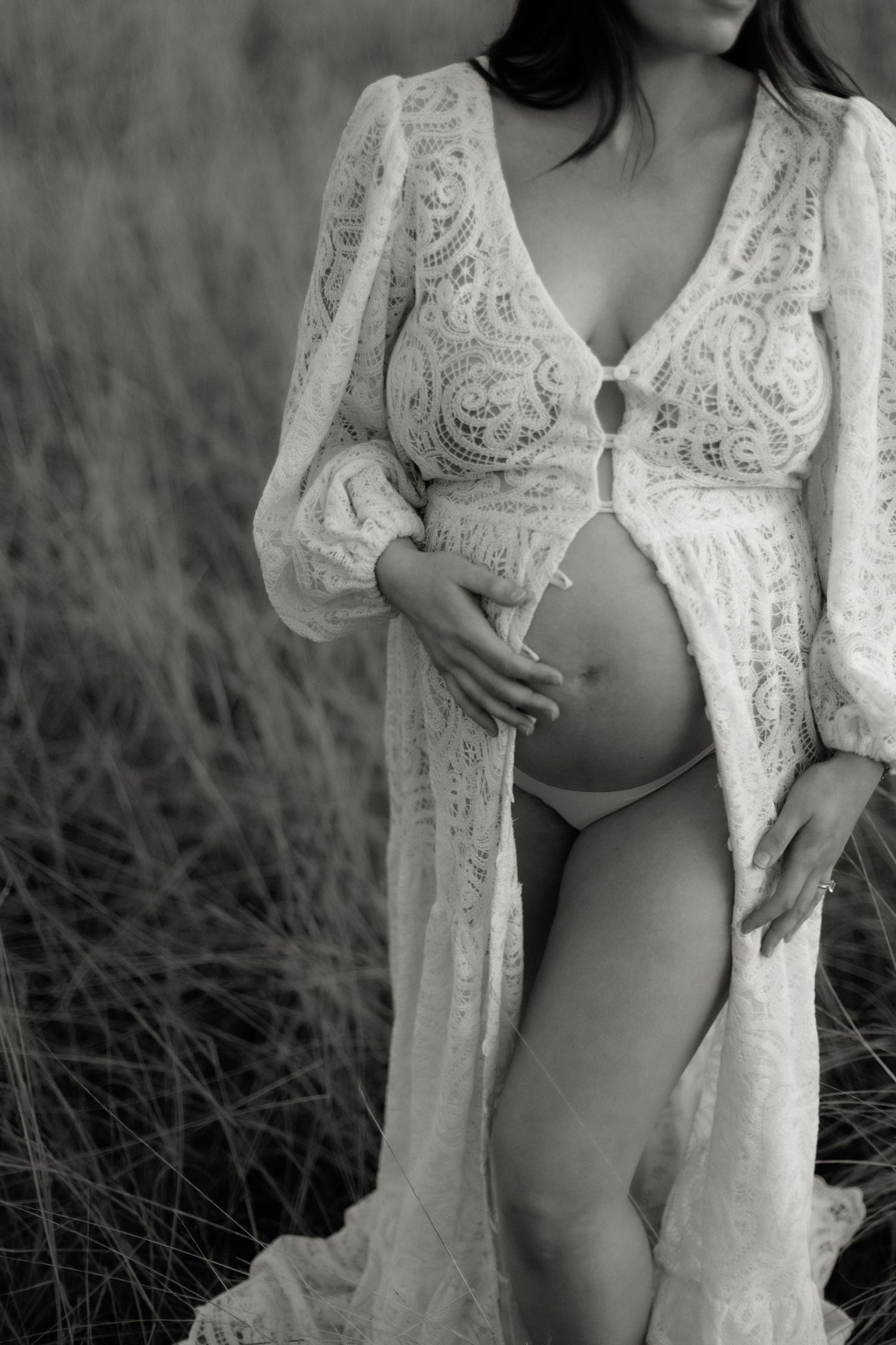 Black and white close-up of pregnant woman in lace robe cradling baby bump.