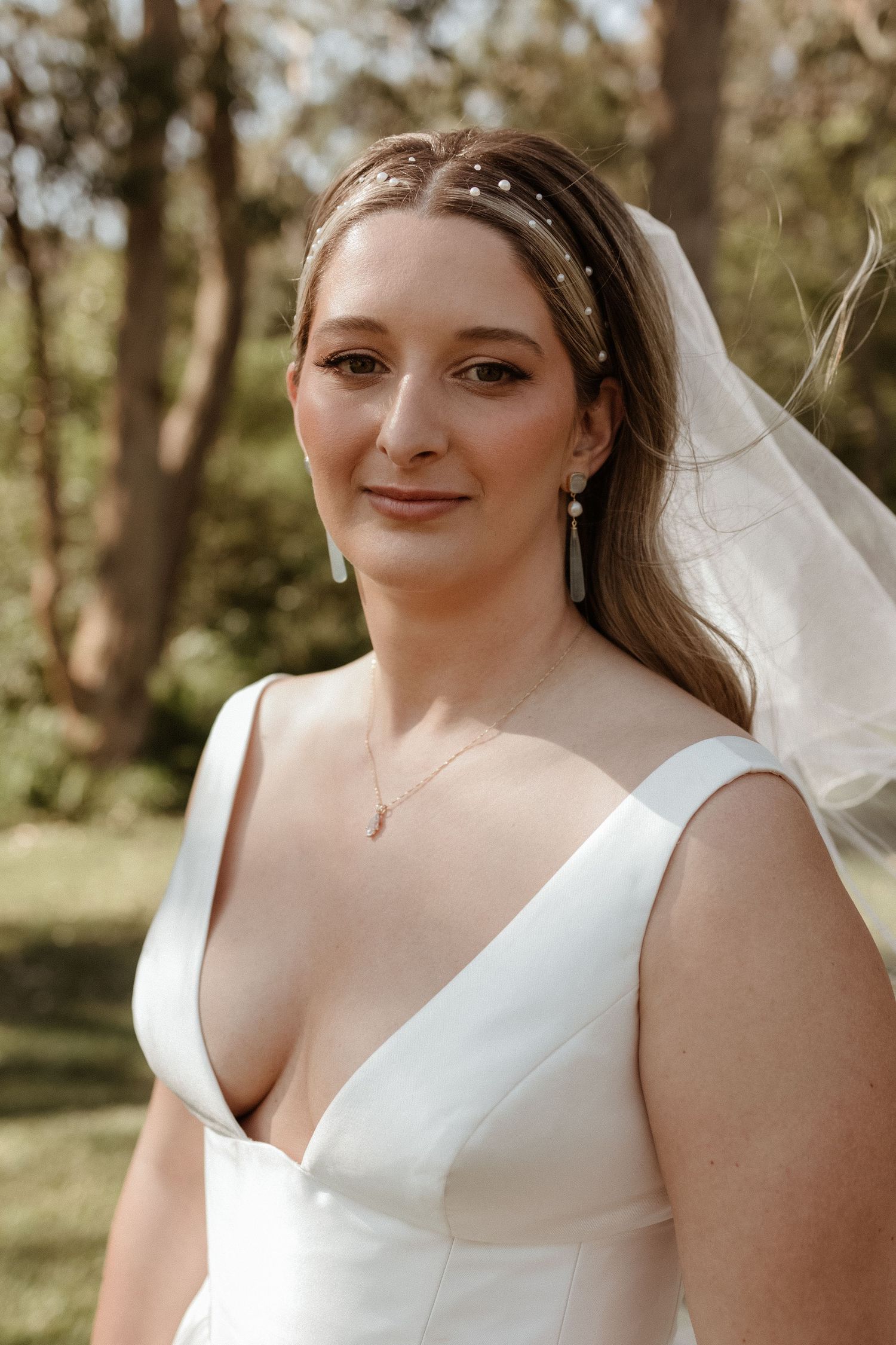 Close-up portrait of a smiling bride wearing a pearl headband, veil, and elegant drop earrings.