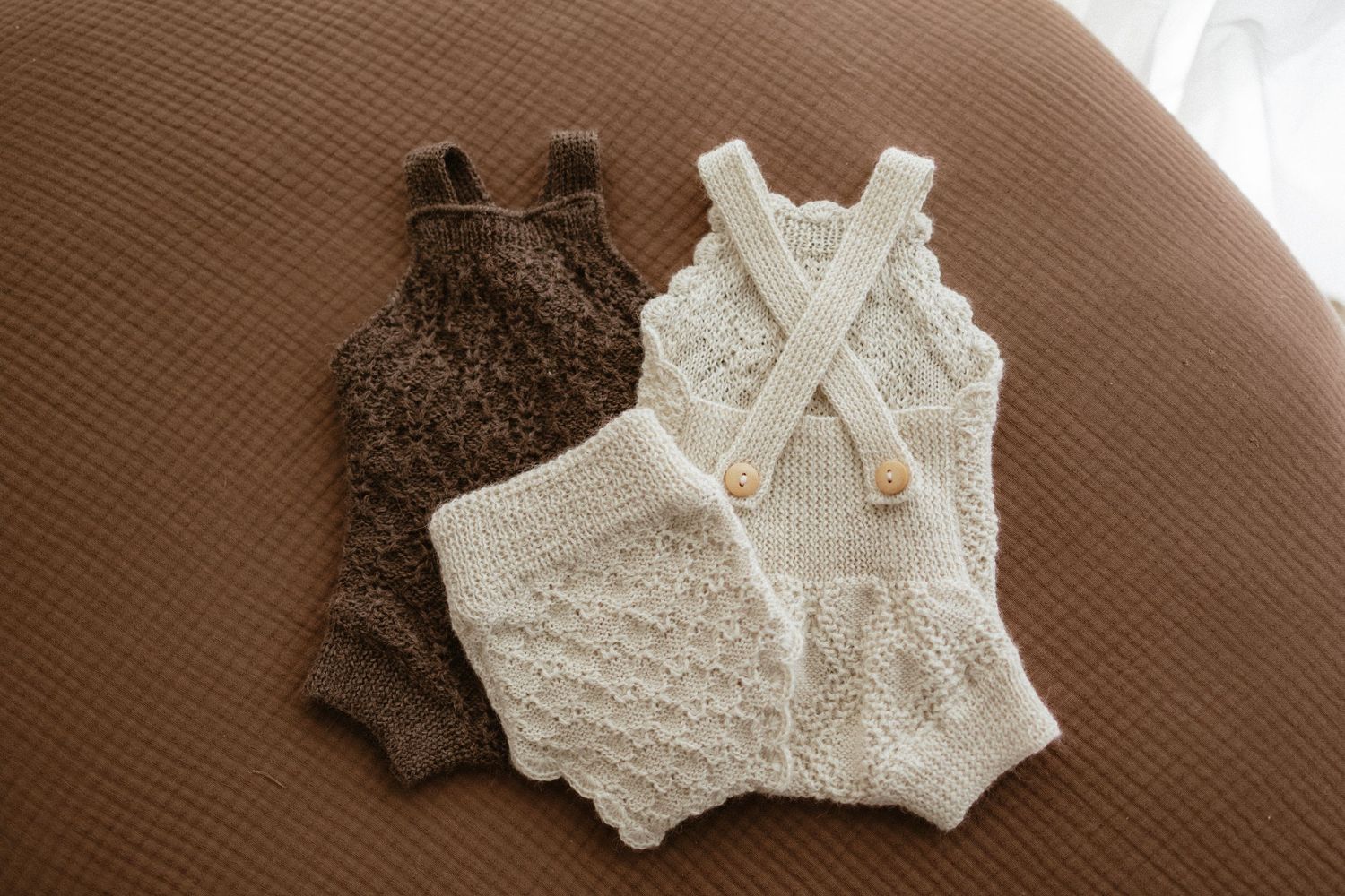 Two handmade crochet baby rompers in brown and cream displayed on a brown surface.