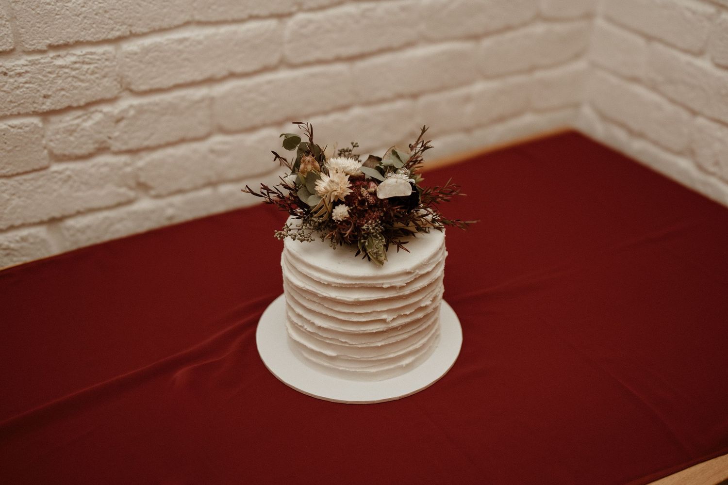 Single-tier white textured wedding cake topped with burgundy and dried floral arrangement.