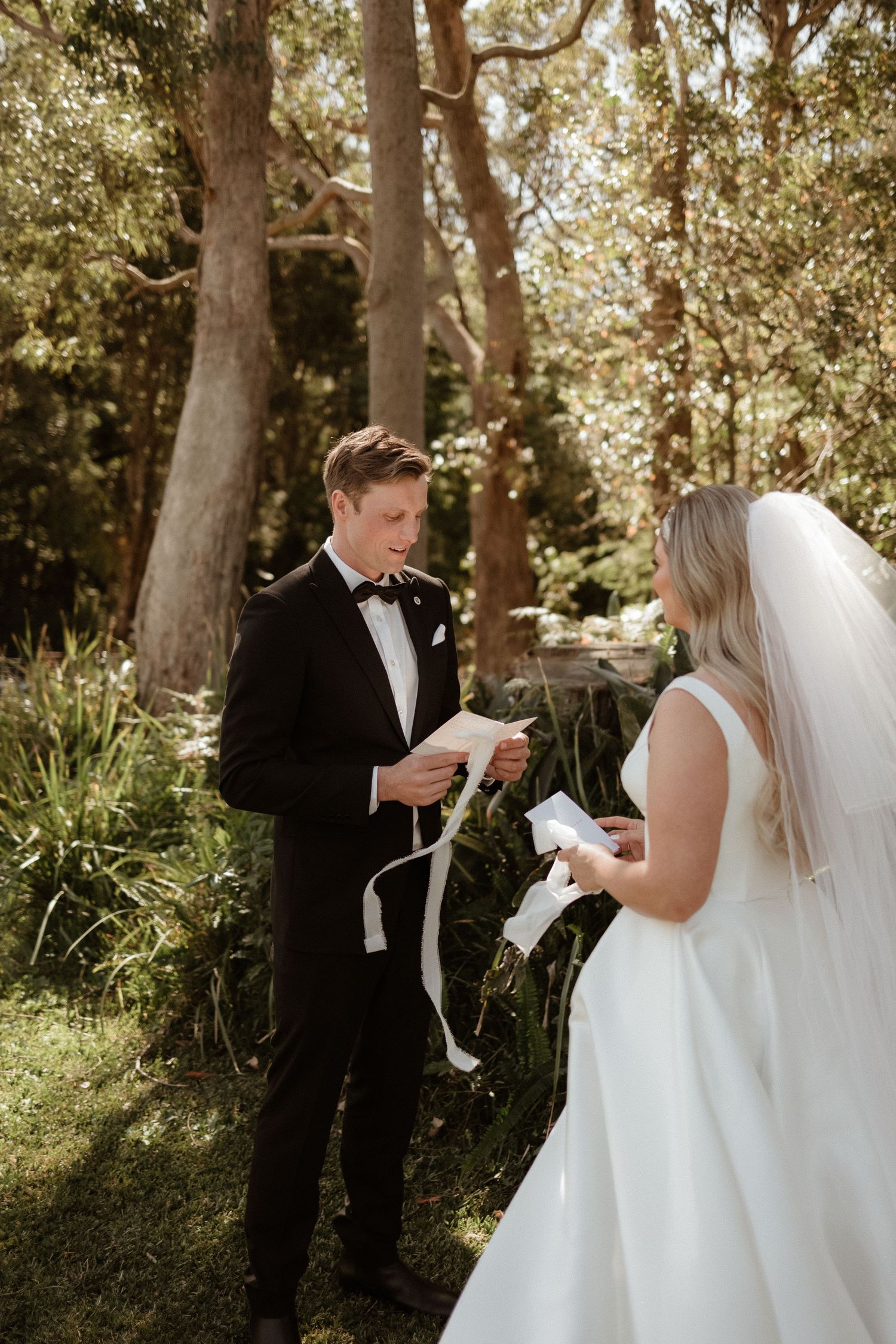 Bride and groom exchanging personal vows outdoors in a lush green forest setting on their wedding day.