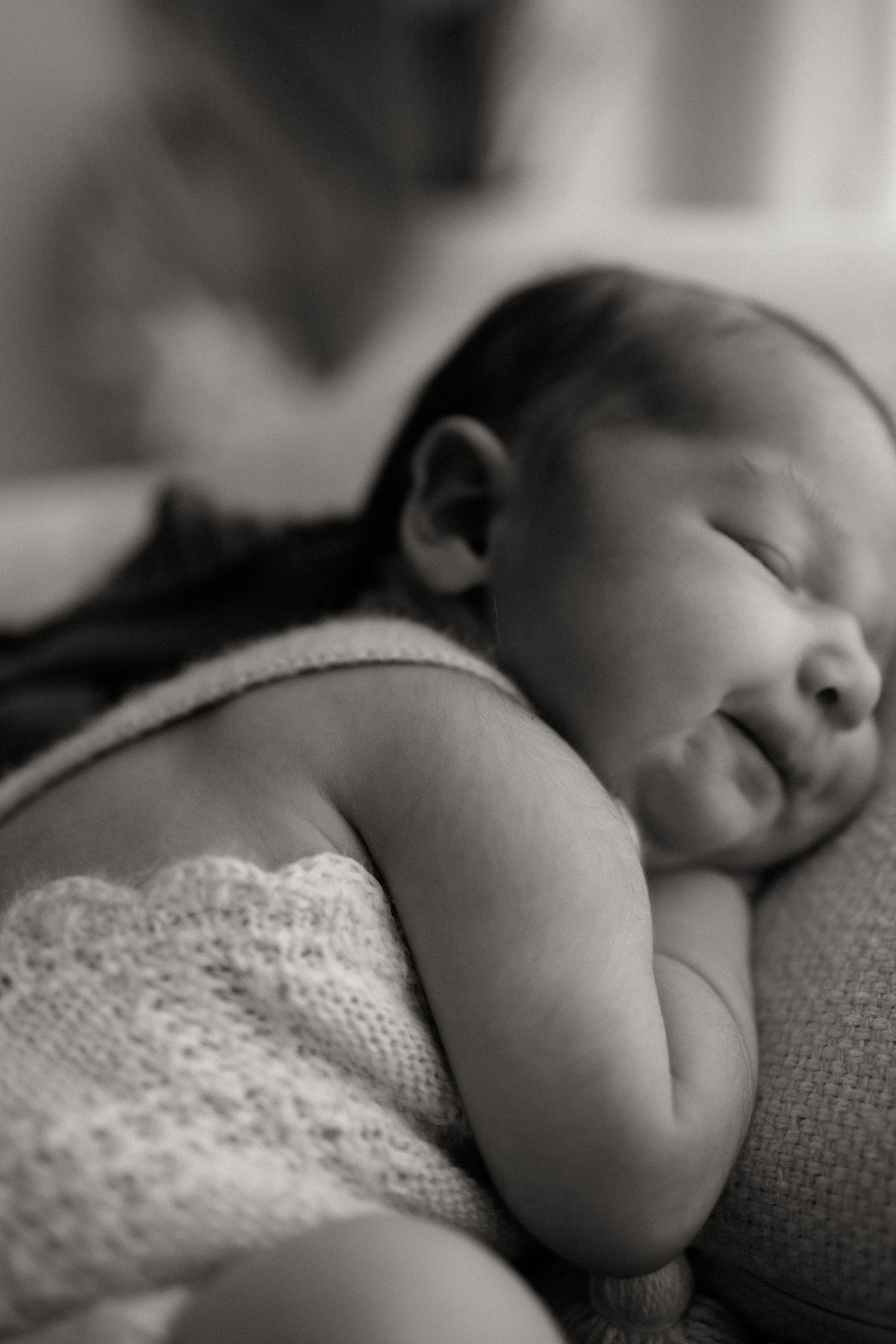 Black and white close-up portrait of a peacefully sleeping newborn baby wrapped in lace blanket.