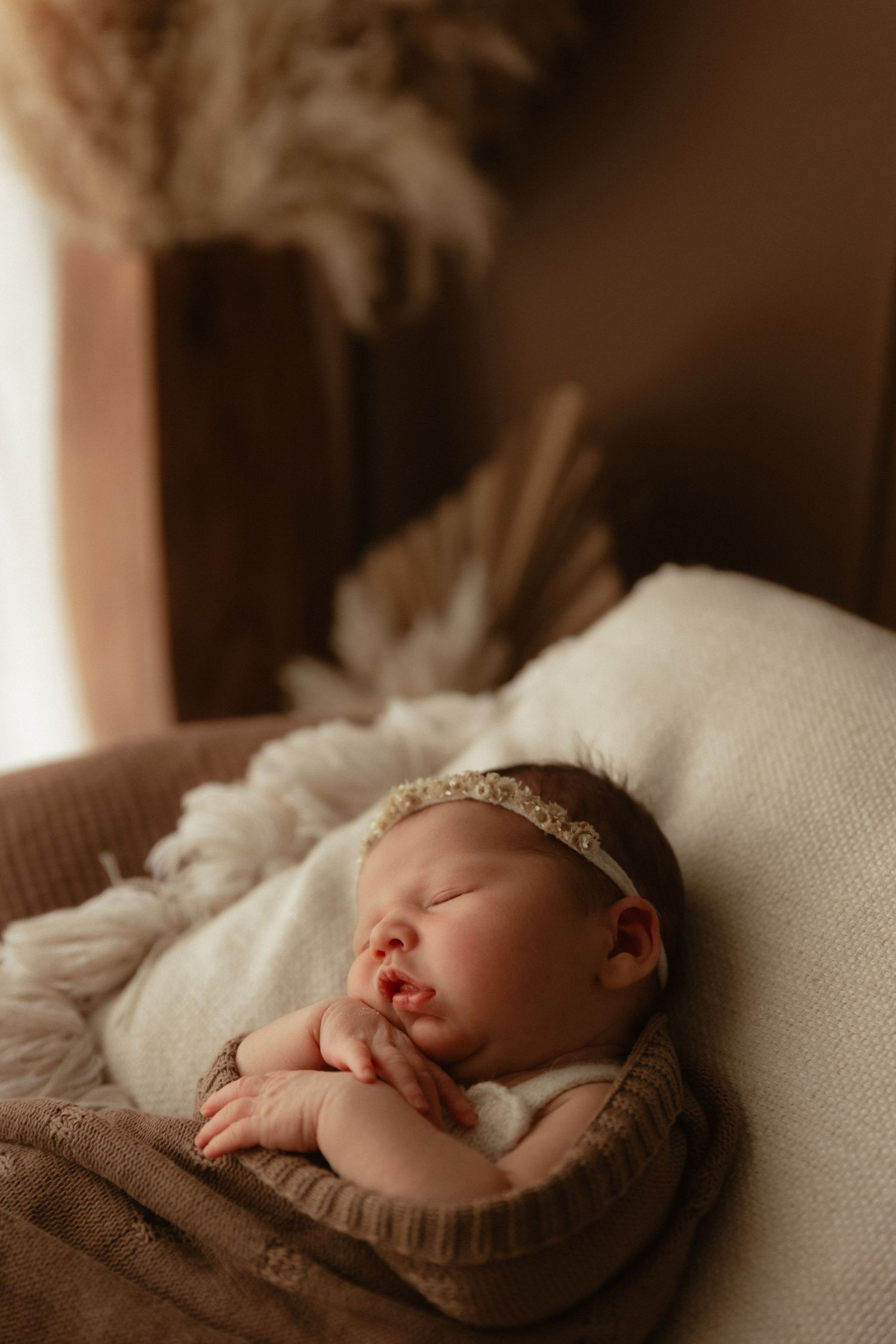 Newborn baby girl sleeping peacefully in a basket wearing a delicate headband, wrapped in soft cream blankets.