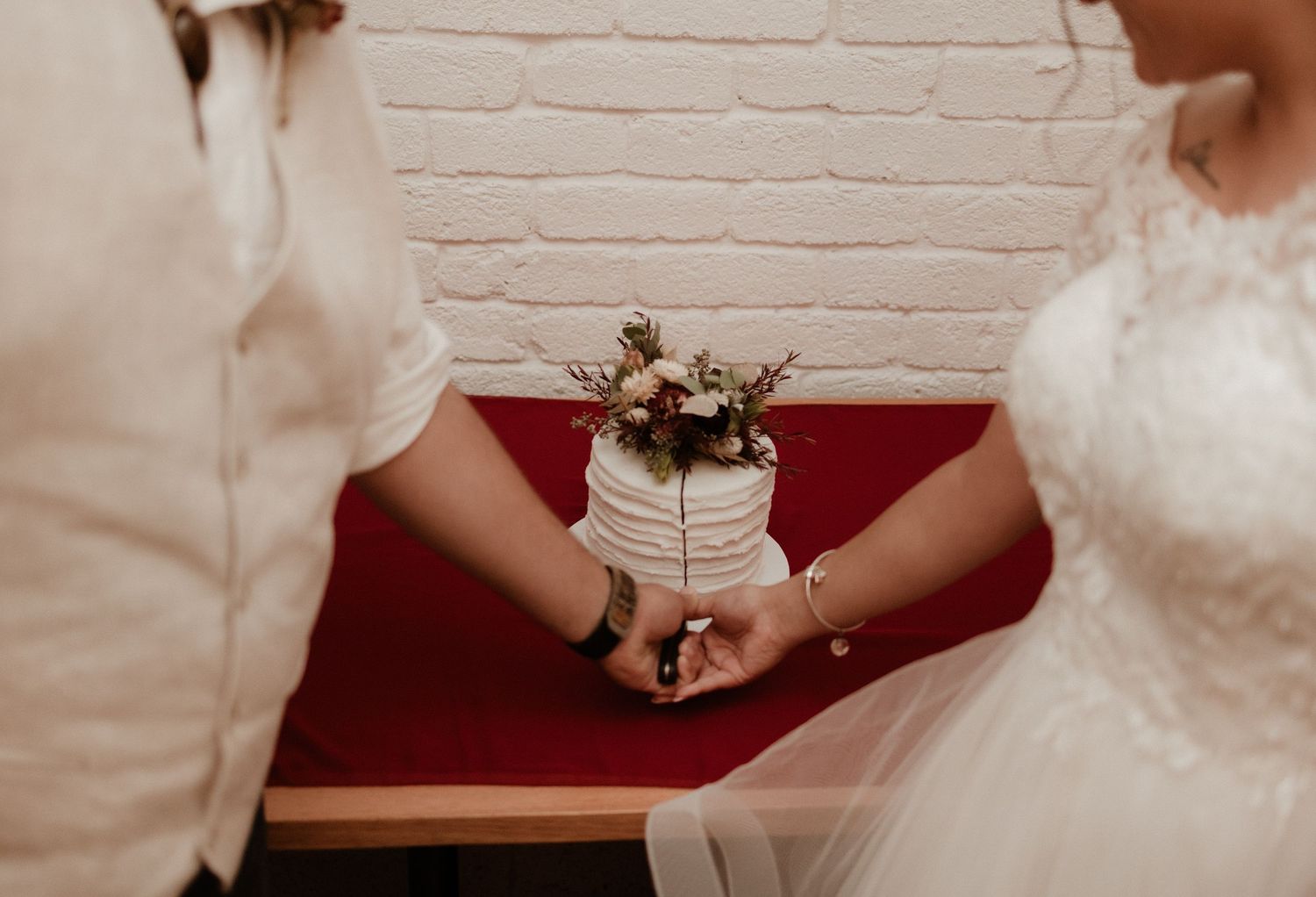 Bride and groom cutting a small white textured wedding cake decorated with dried flowers together.