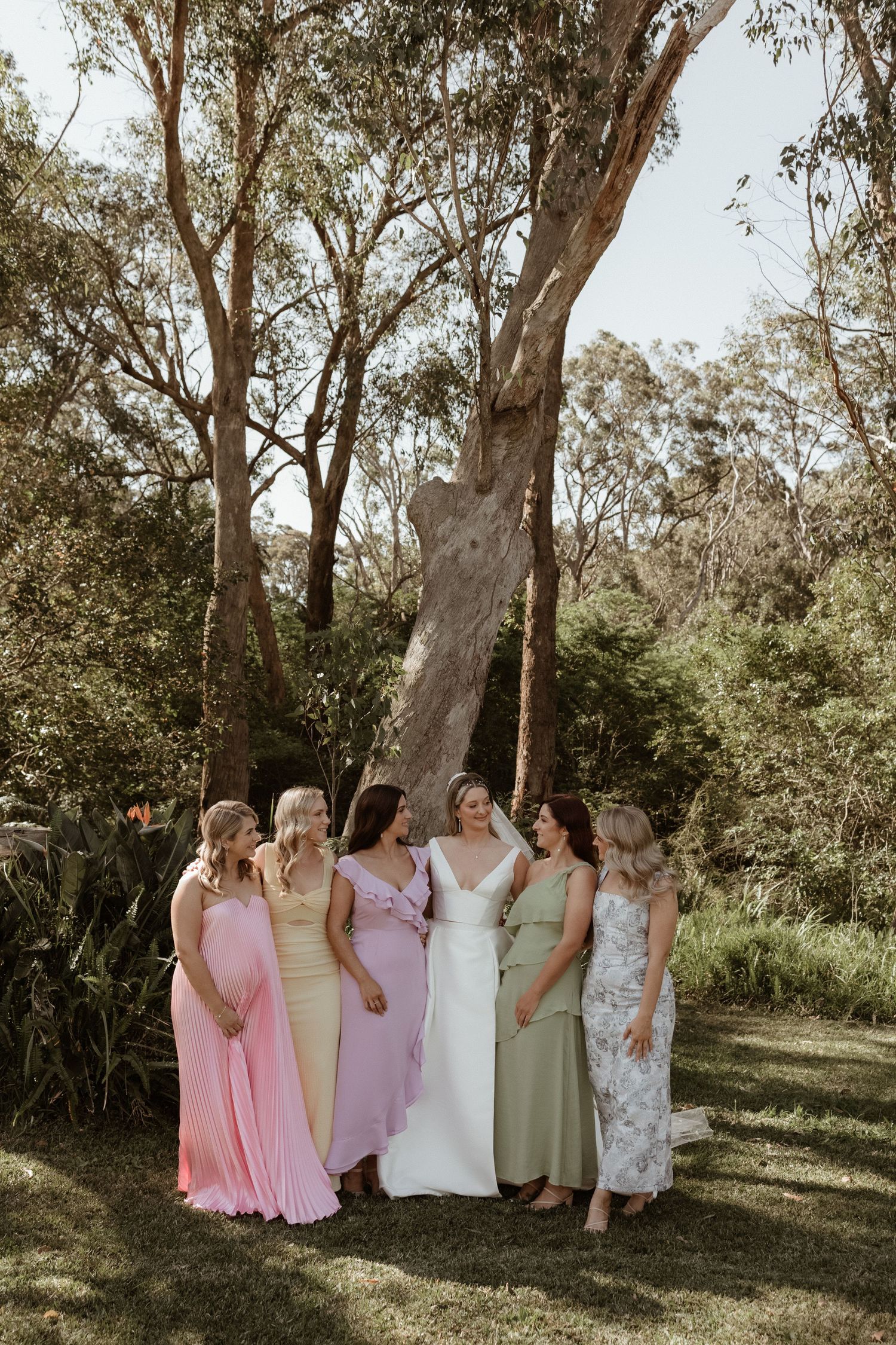 Bride and bridesmaids in colorful pastel dresses laughing in a garden.