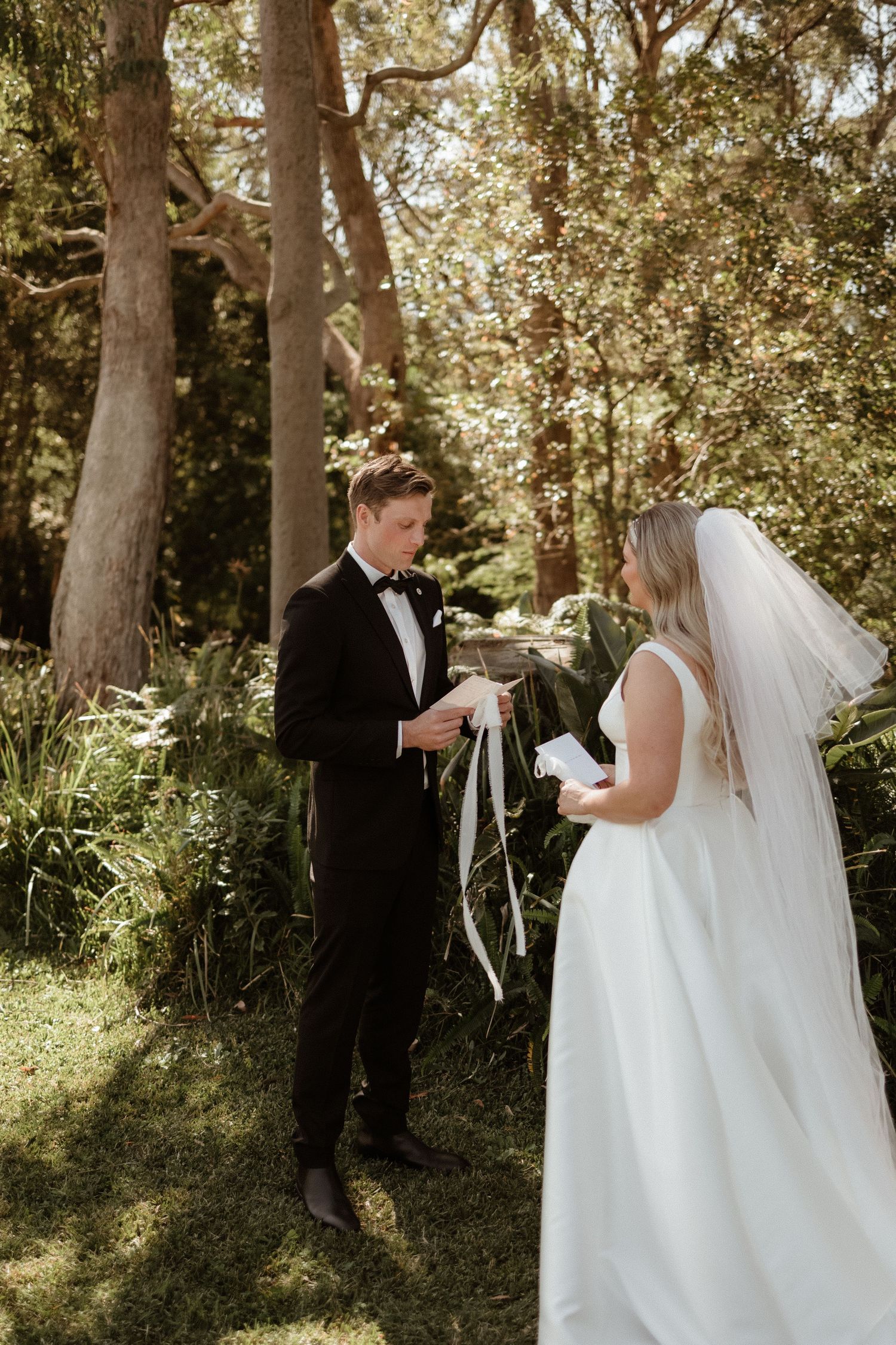 Groom reads wedding vows to bride in a lush green forest ceremony setting.