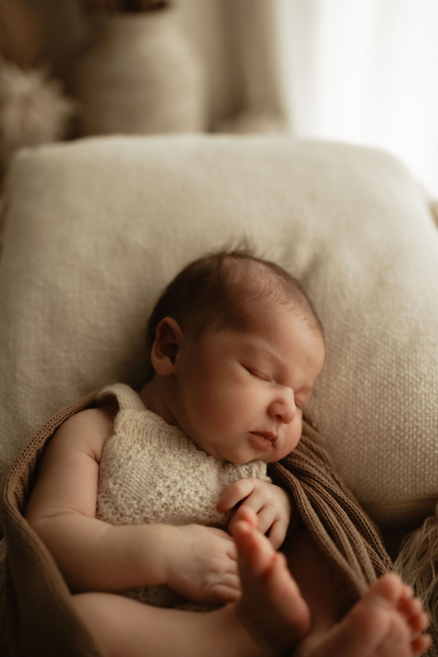 newborn baby sleeping wearing a cream knit romper, soft natural light photography.