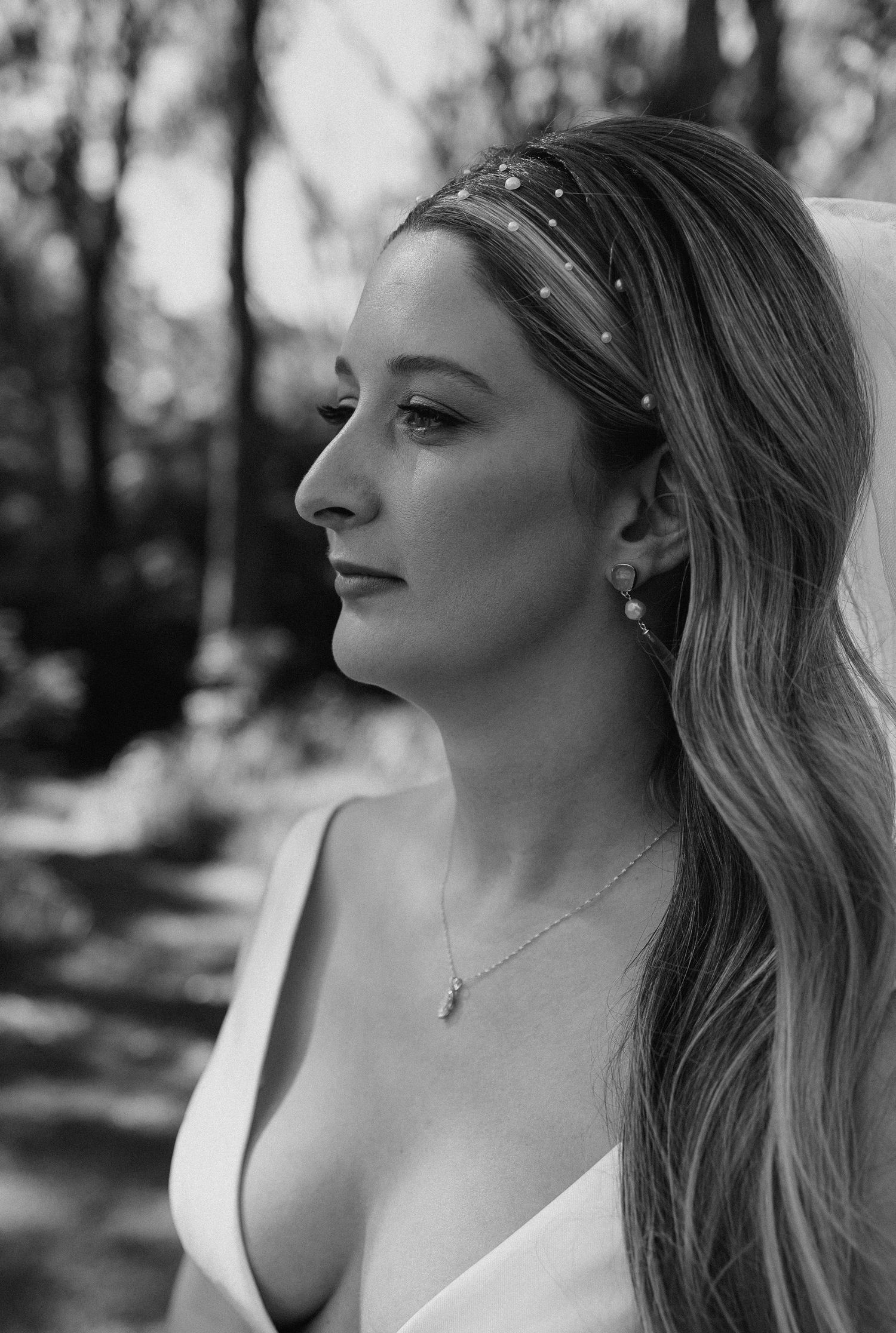 Black and white bridal portrait of a woman in a white dress with pearl headband and necklace, hair flowing softly.