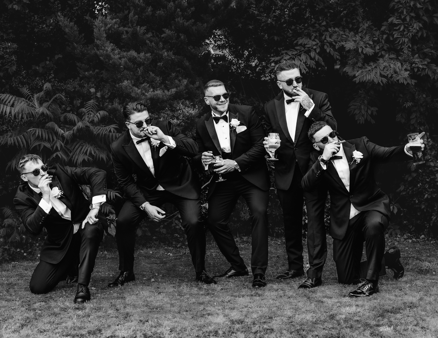 Wedding party relaxing casually on grass in formal attire.